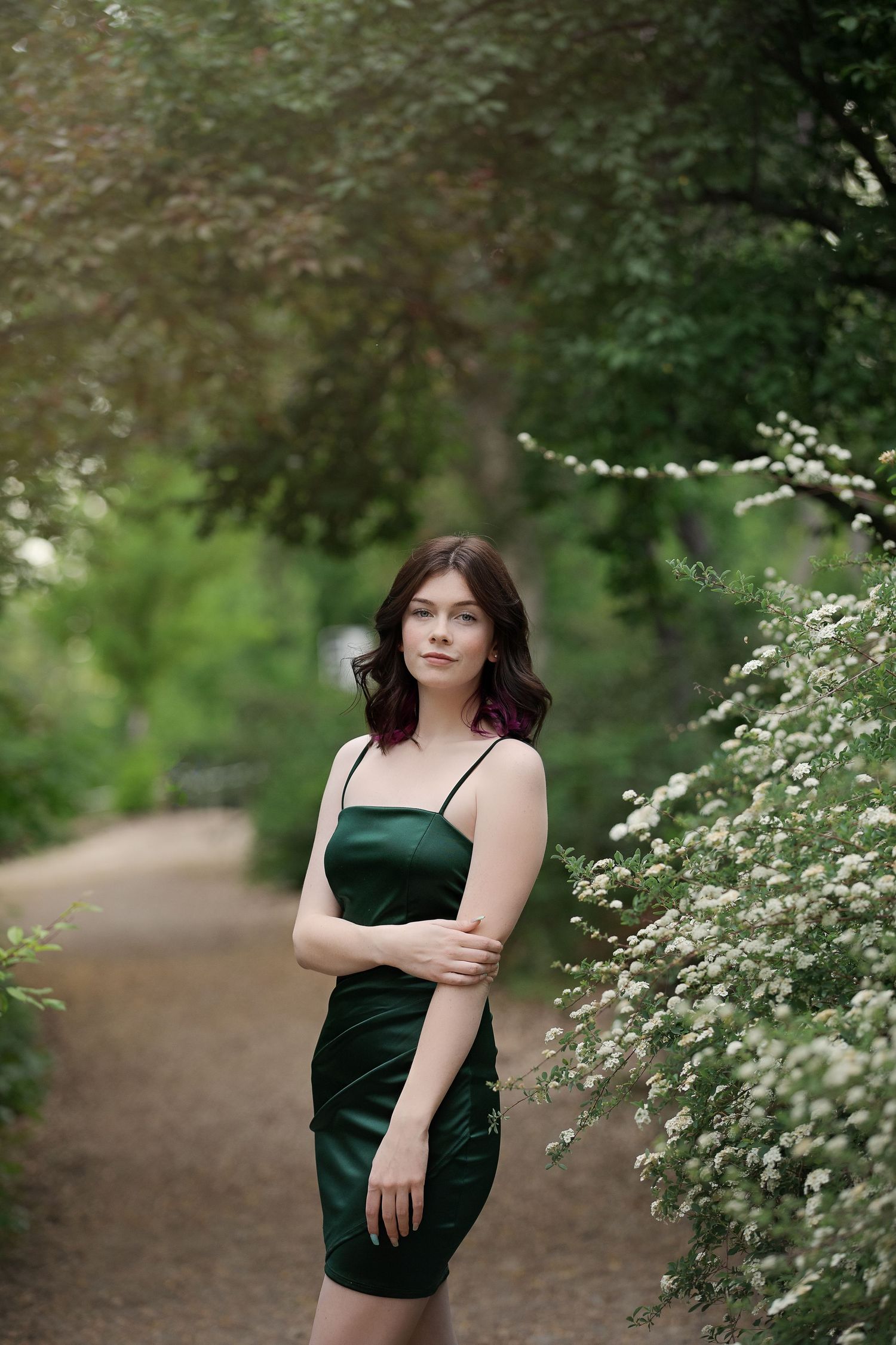 Outdoor portrait on garden path wearing emerald green dress surrounded by white flowering bushes.