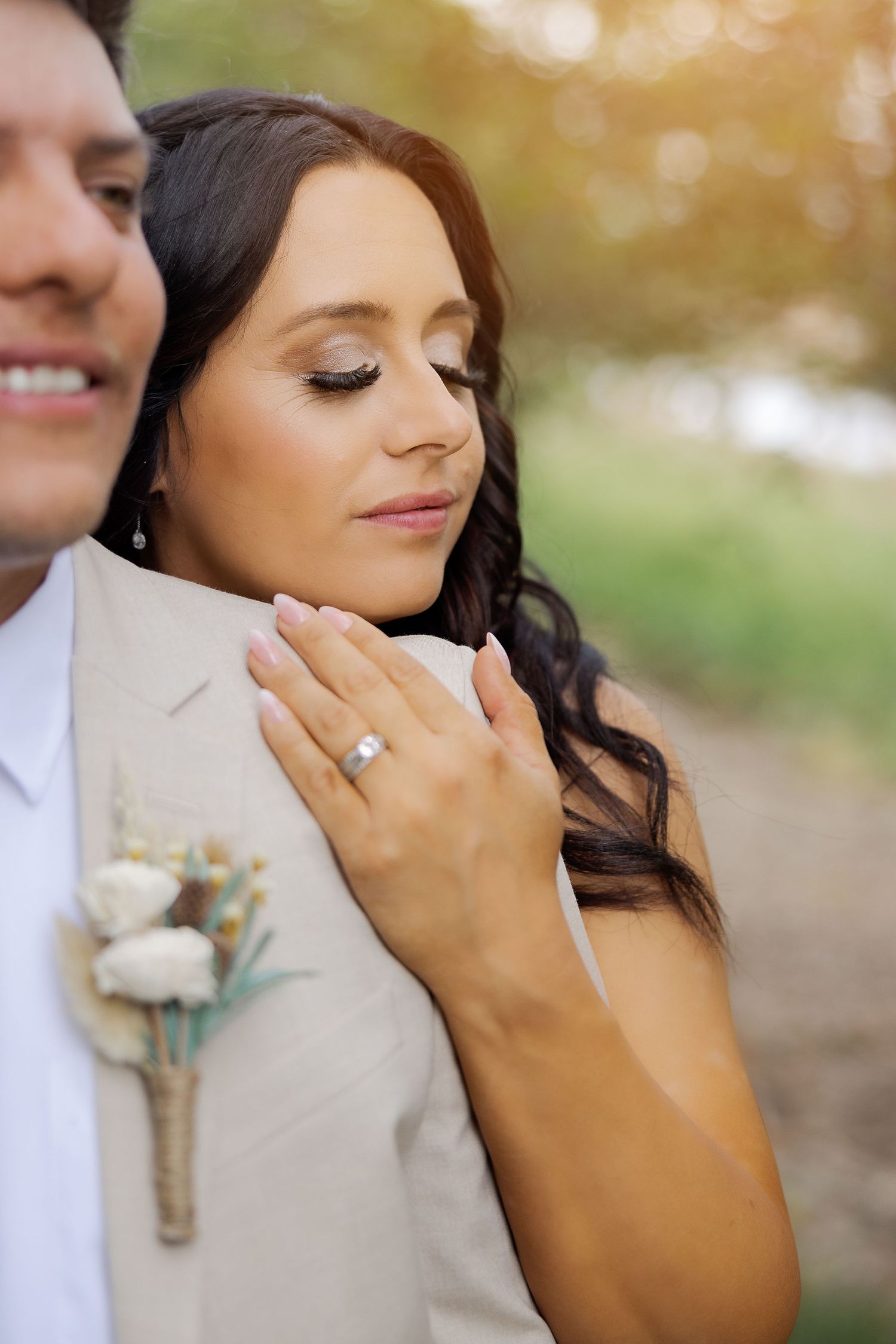 Romantic wedding portrait showing diamond ring and boutonniere detail in golden light.