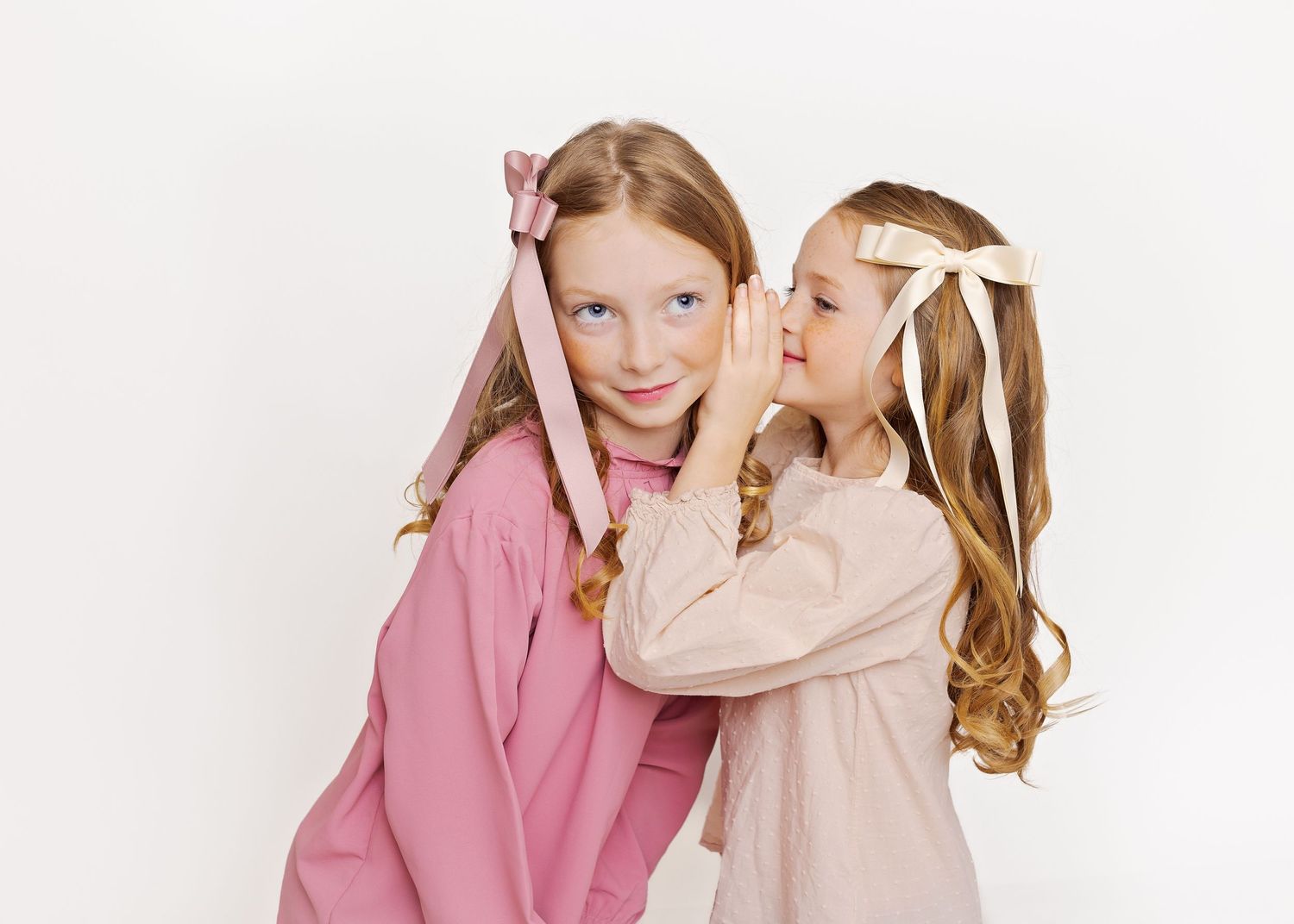 Two young friends in pink and beige dresses sharing secrets and giggles.