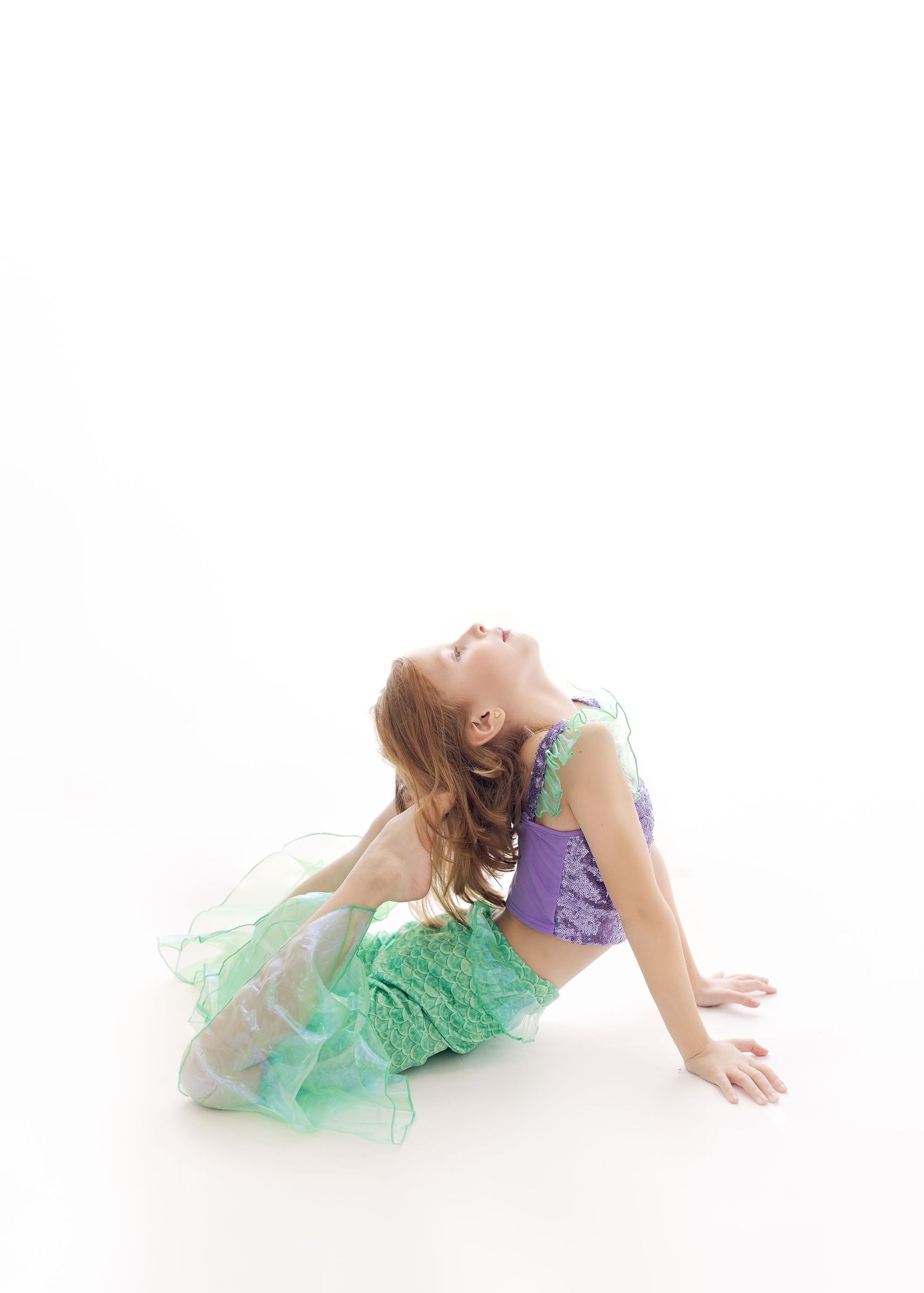 Dancer in green tulle skirt and purple leotard performs graceful pose against white background.