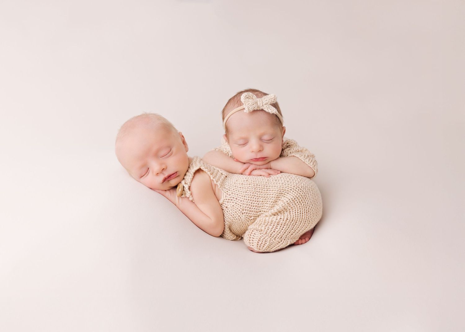 Sweet newborn baby sleeping peacefully in cream knitted wrap on soft beige backdrop in artistic photography style.