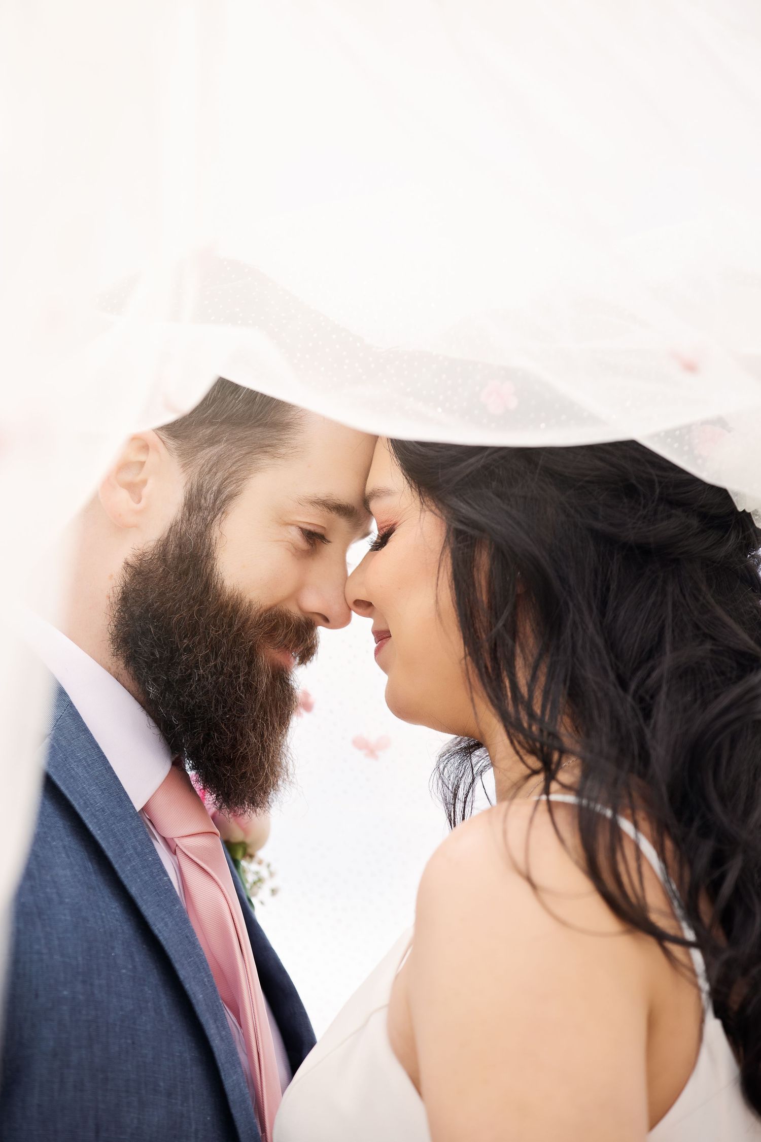 Intimate wedding portrait under sheer veil showing tender romantic moment.