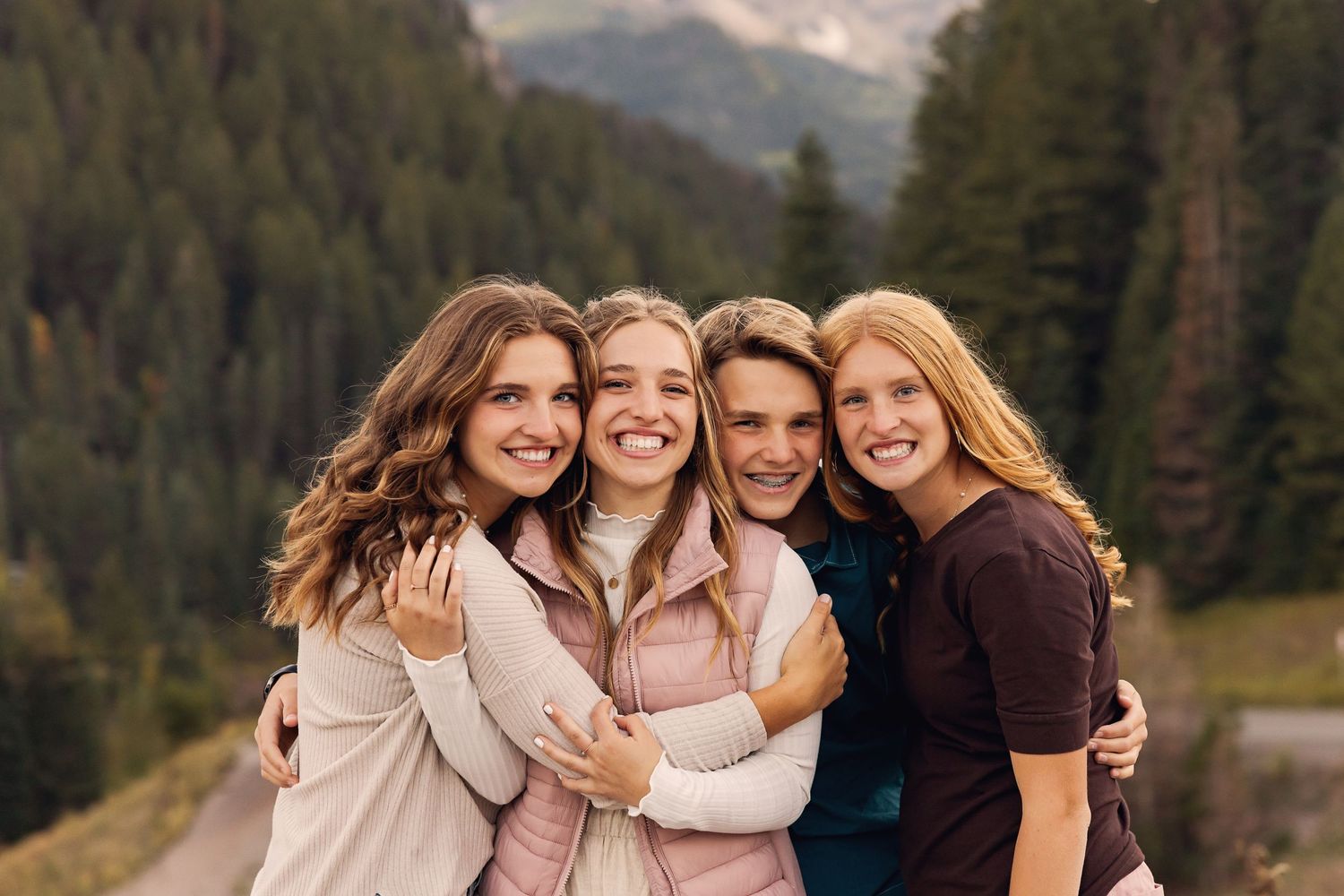 Friends embrace while posing for photo with mountain forest landscape in background.
