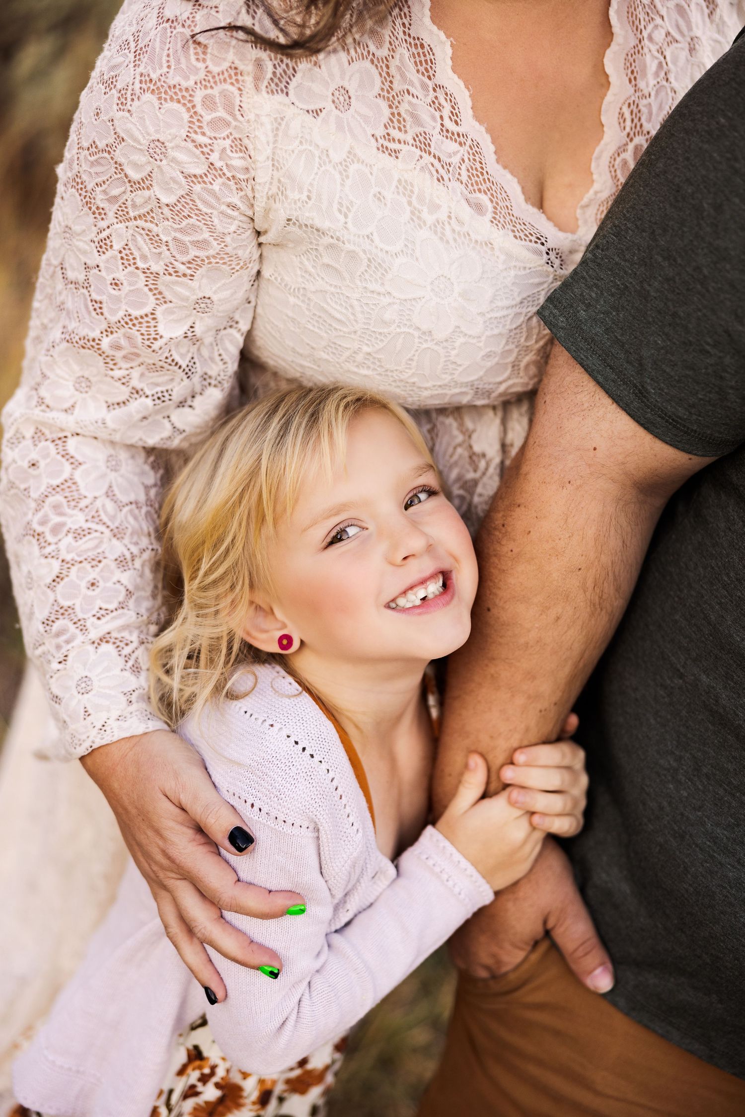 A sweet family moment with a small child hugging between two adults in formal attire.