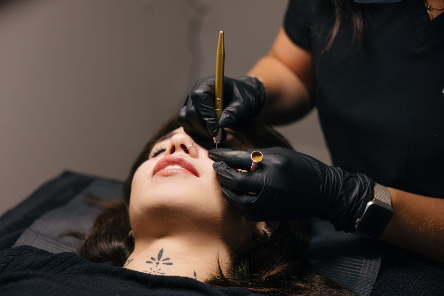 Closeup of someone receiving a professional eyebrow microblading treatment with black gloved hands holding tools. Montreal, rive sud
