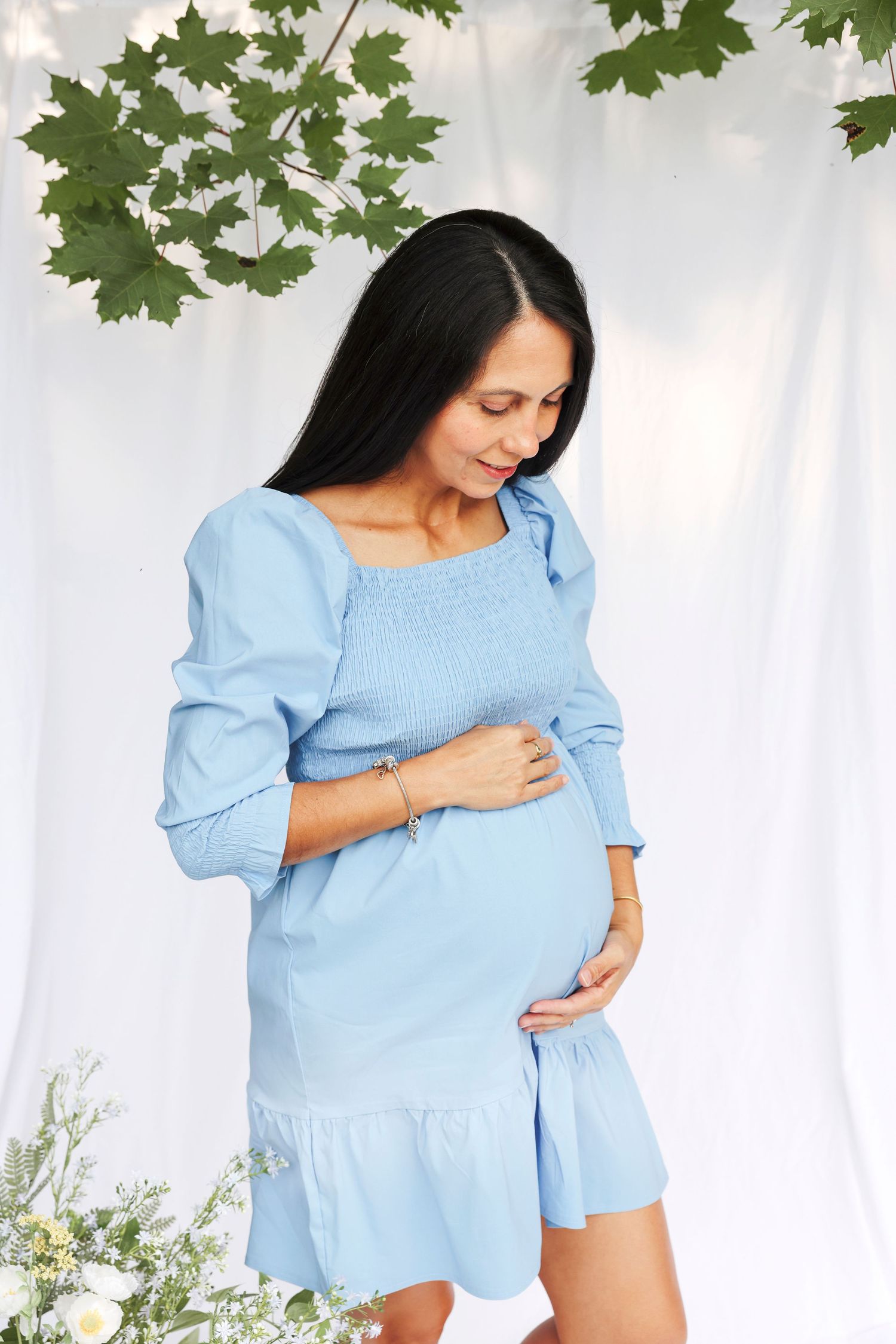 Woman in light blue puff sleeve dress poses against white backdrop with green foliage accents.