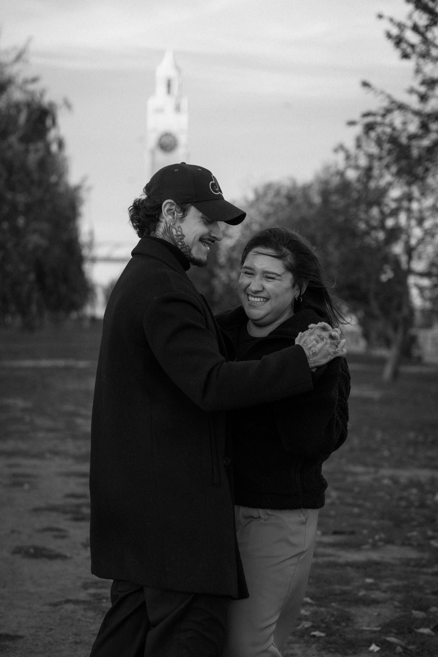 A couple shares an intimate moment dancing together outdoors during sunset in black and white photography.