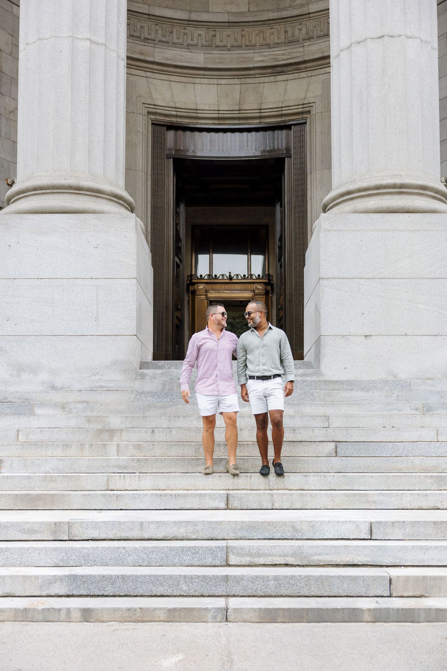 Two people sit together on white marble steps of a grand building with classical columns.