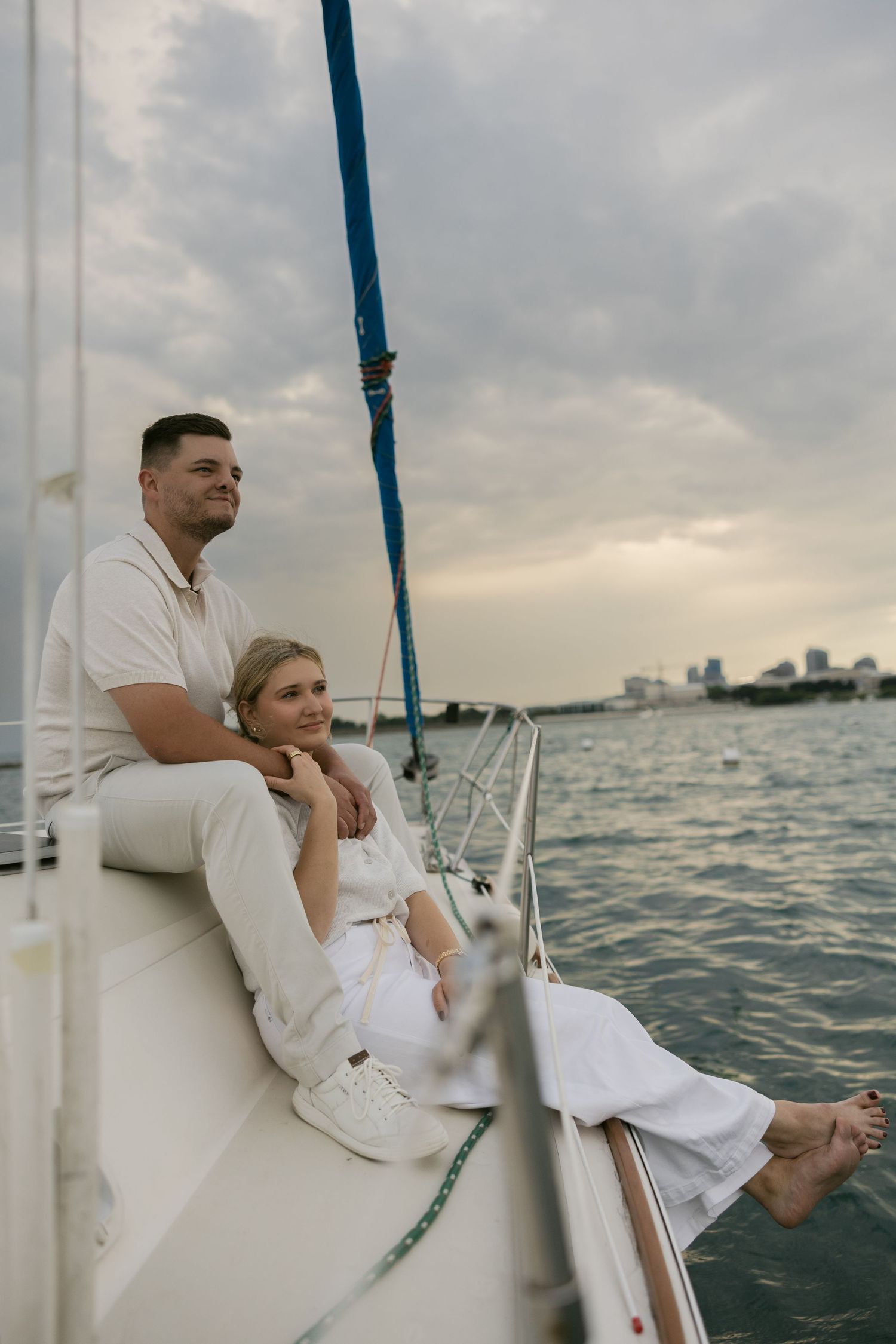 A couple dressed in white enjoys a romantic moment together on a sailboat at sunset.