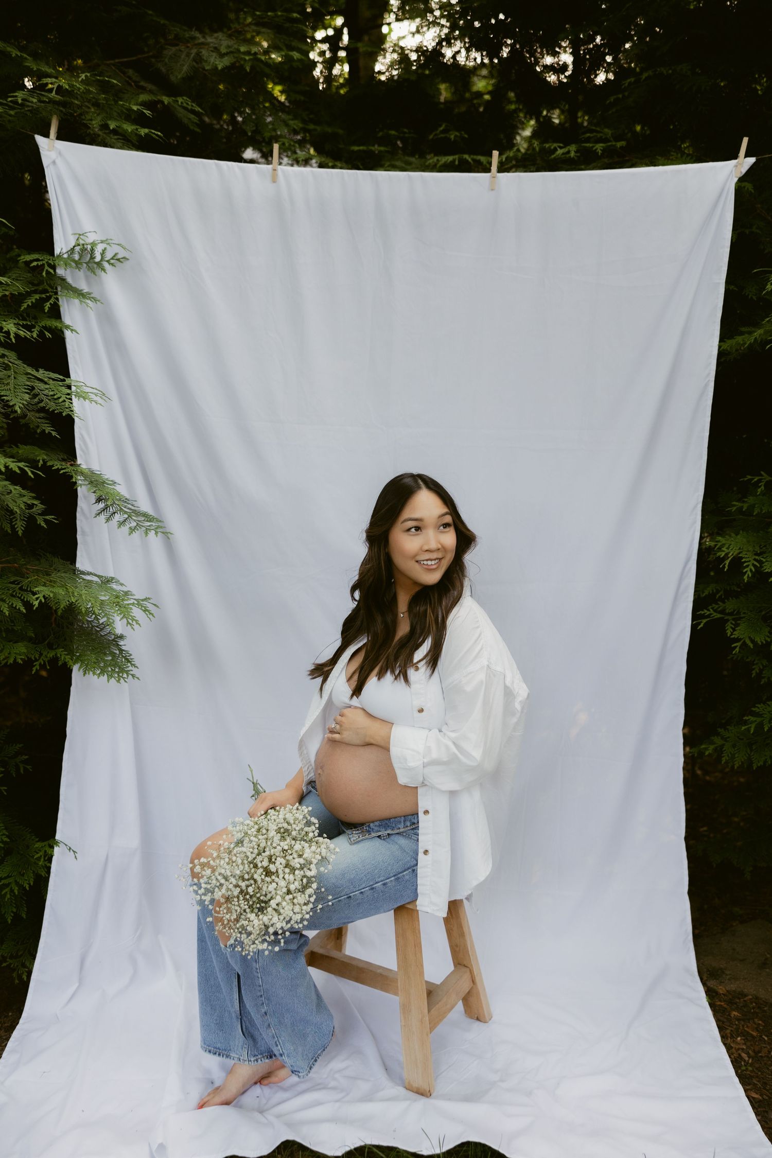 Natural light maternity photography with white backdrop and forest background.