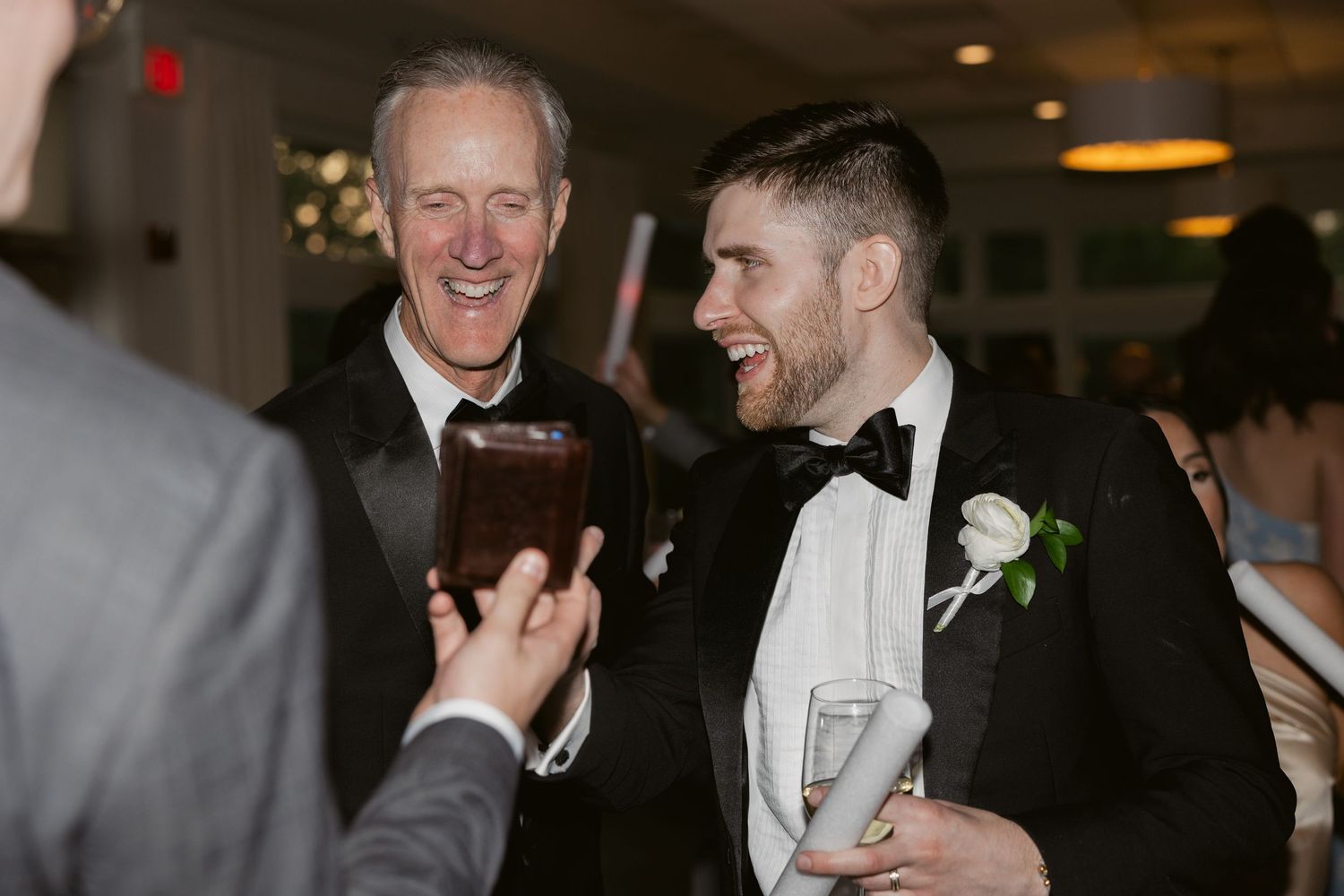 Wedding guests in formal attire share laughter and conversation at an evening reception.