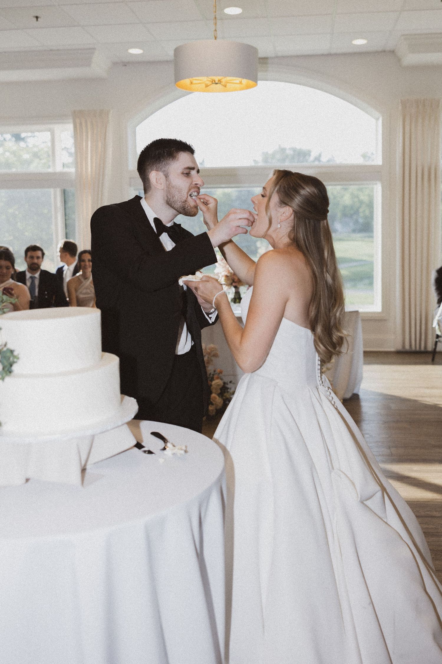 Playful moment as newlyweds feed each other wedding cake at reception.