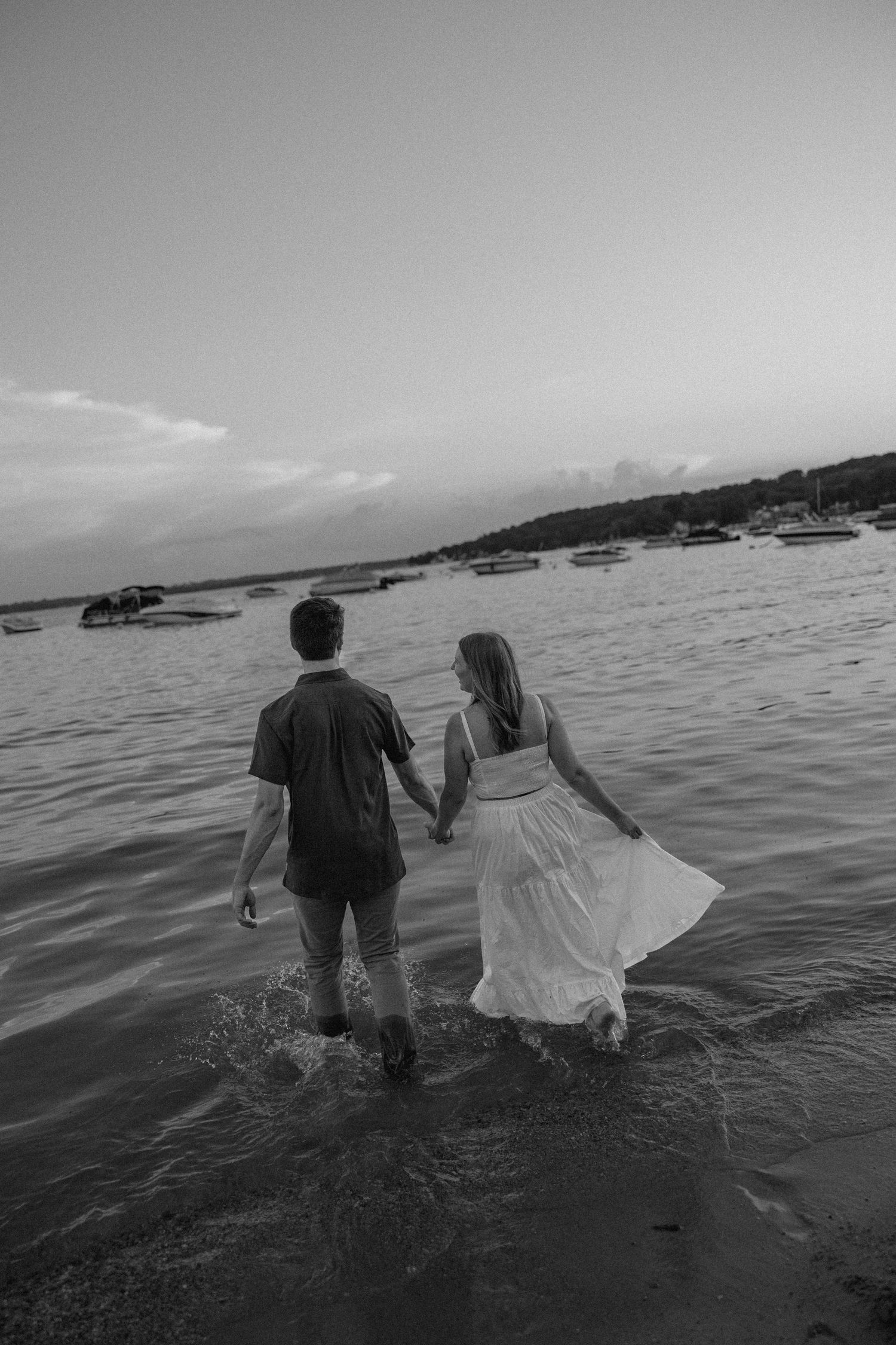Black and white photo of couple wading through water at shoreline.