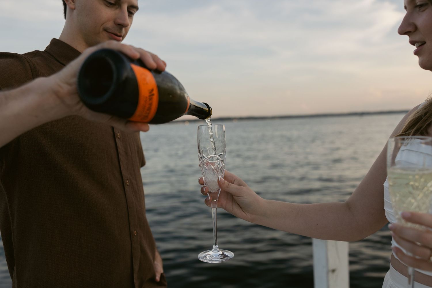 Someone pours champagne into a glass during a sunset boat ride on the ocean.