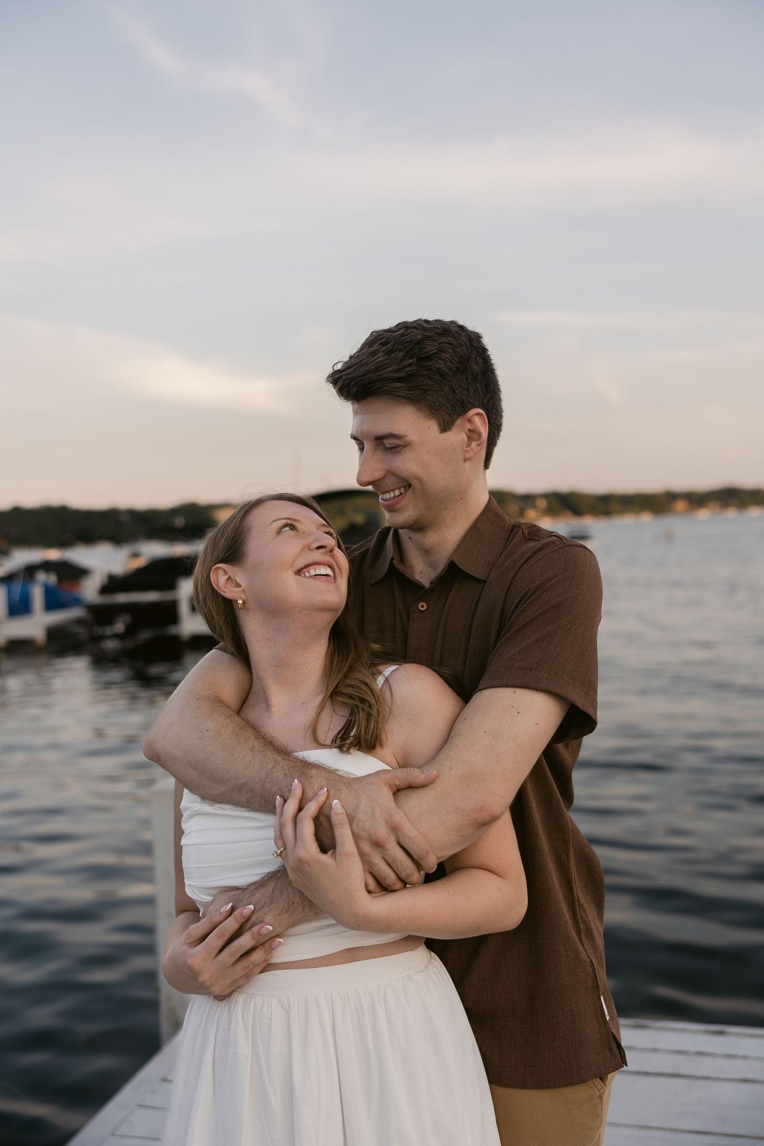 A couple shares a joyful moment while embracing on a wooden dock near the water.