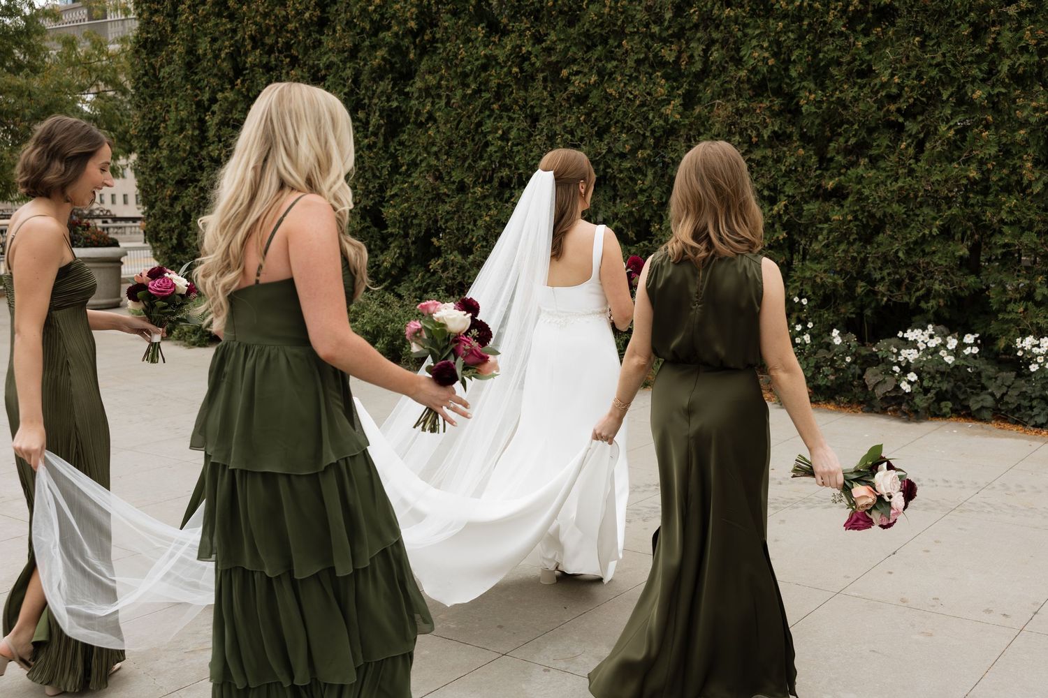 Wedding party members in green dresses and white gowns walk together on a stone pathway.