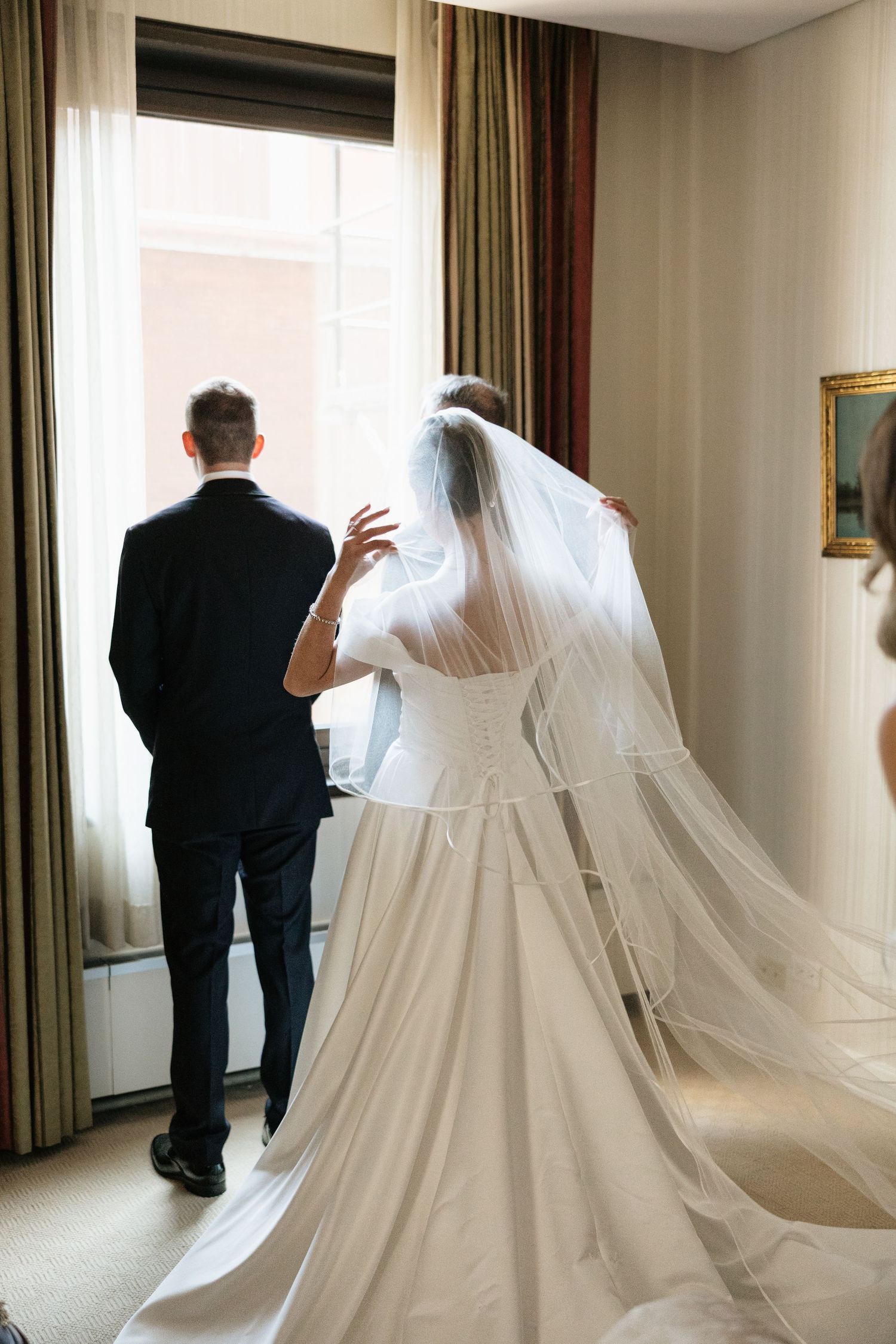 A flowing white wedding dress with long train and veil photographed in a hotel room setting.