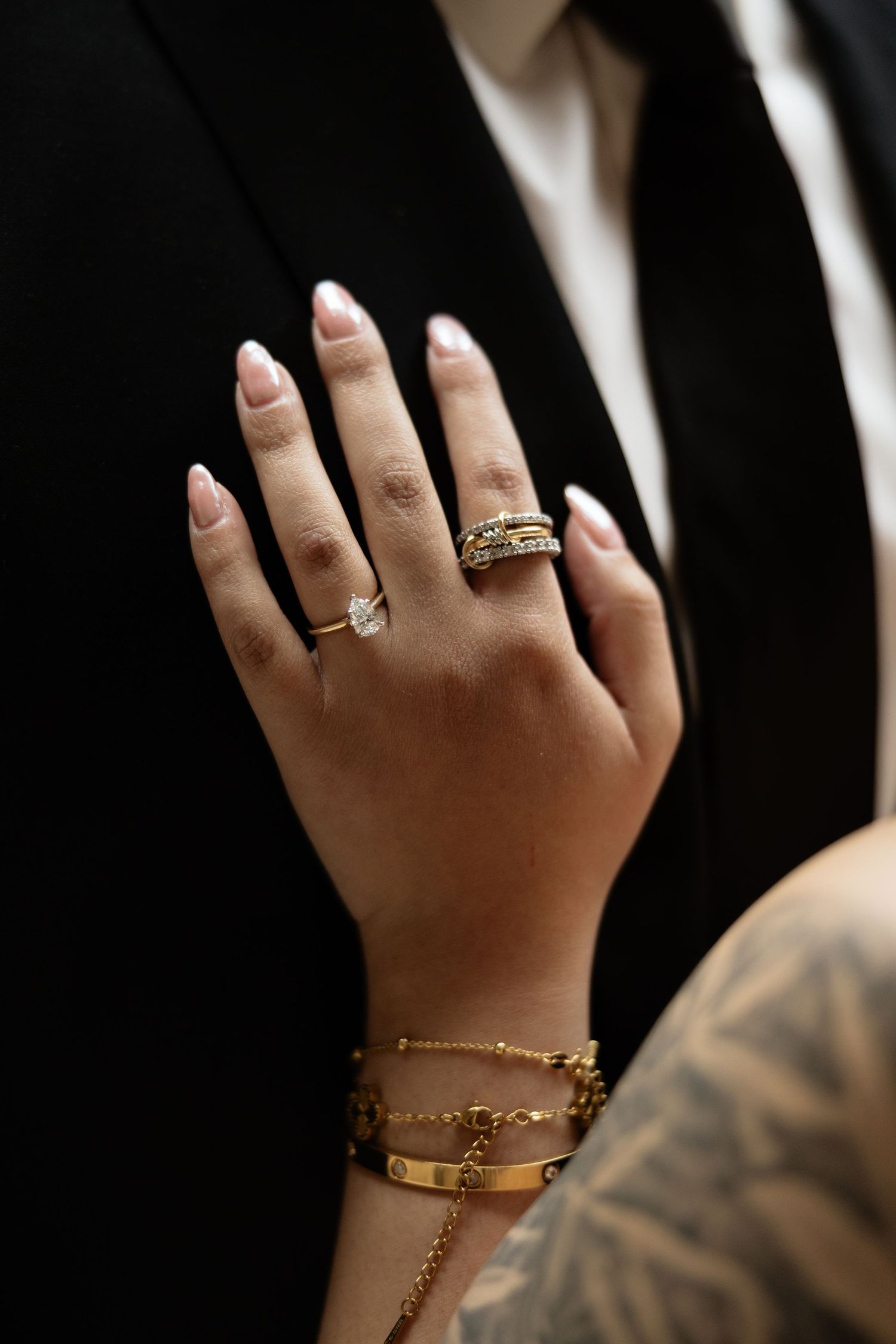 Close-up of a hand adorned with delicate gold jewelry and rings against a black background.
