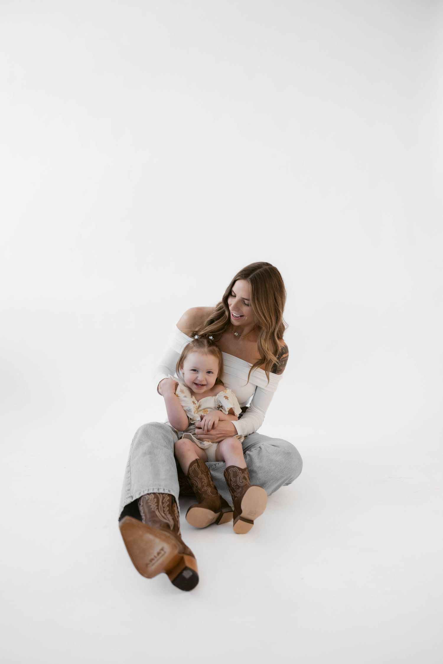 Parent and child share a tender moment in white studio setting, embracing on the floor.