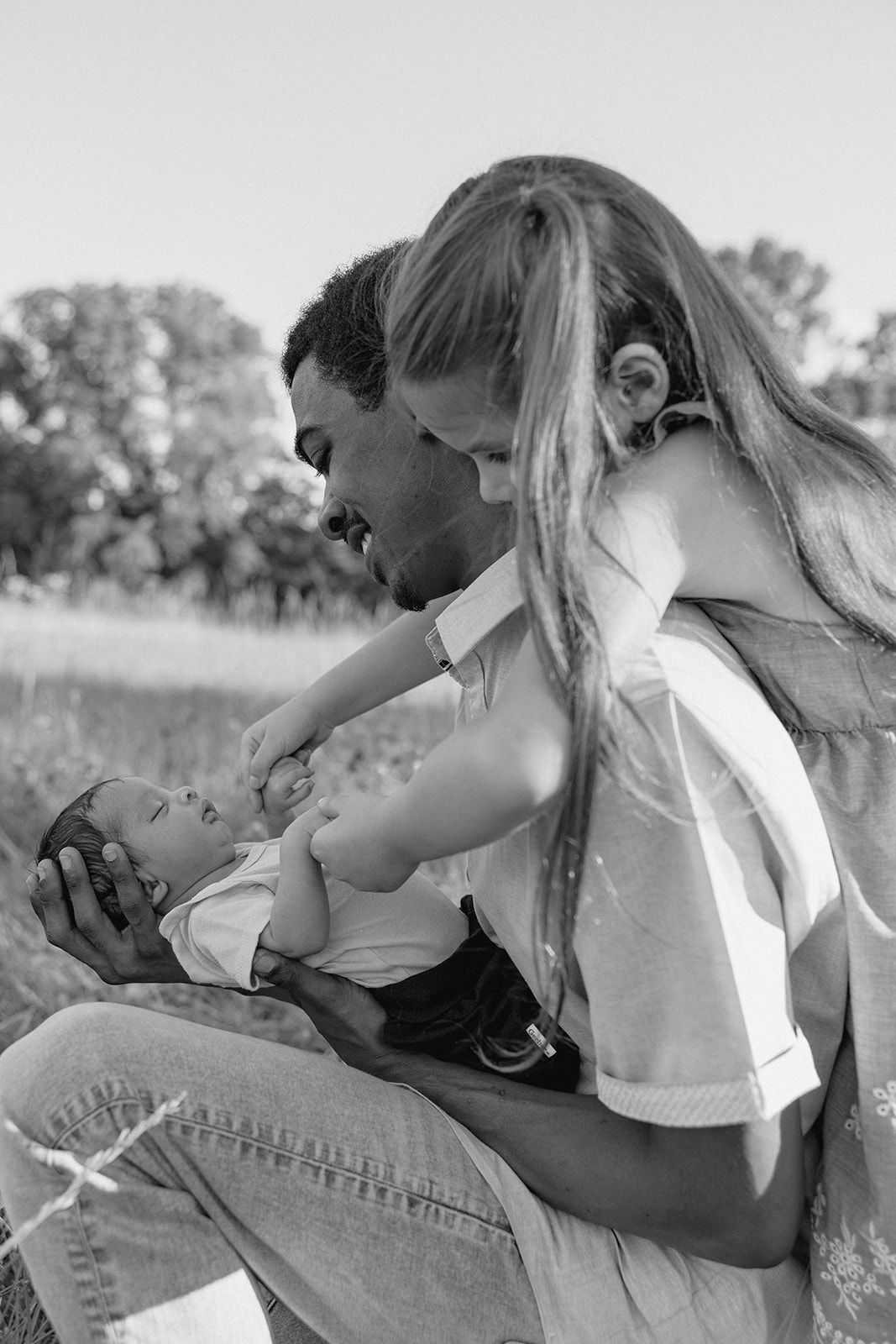 Black and white photo of parents sharing tender moment with baby outdoors.