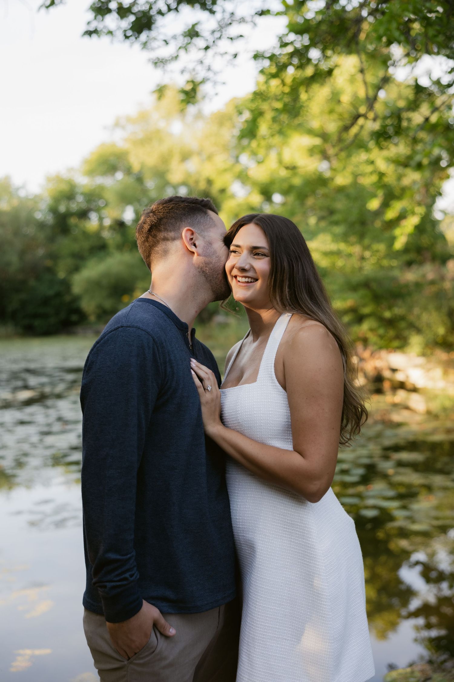 A couple shares a romantic moment by a lake during a sunset photography session.