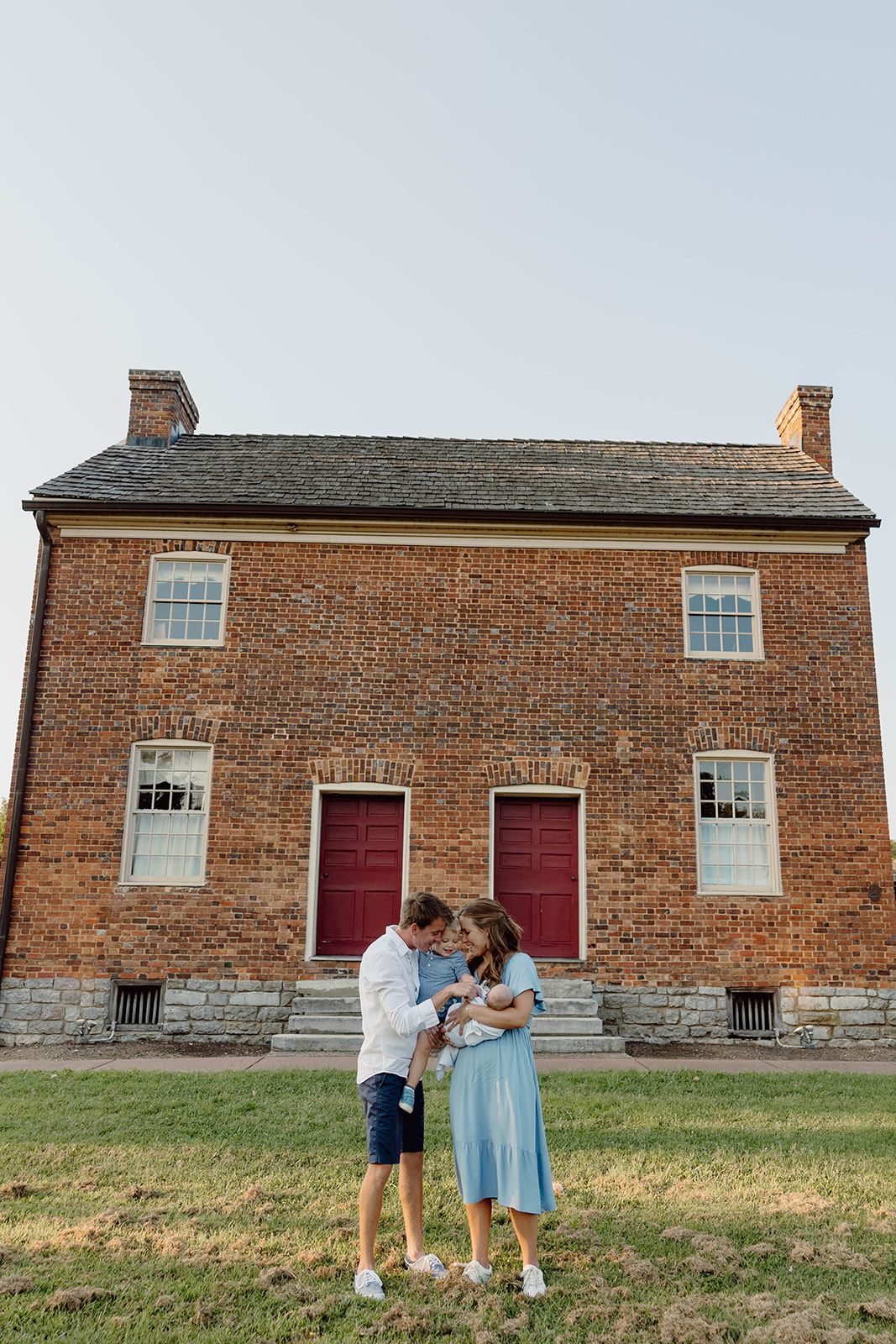 A family shares a tender moment in front of a historic brick building with red doors.