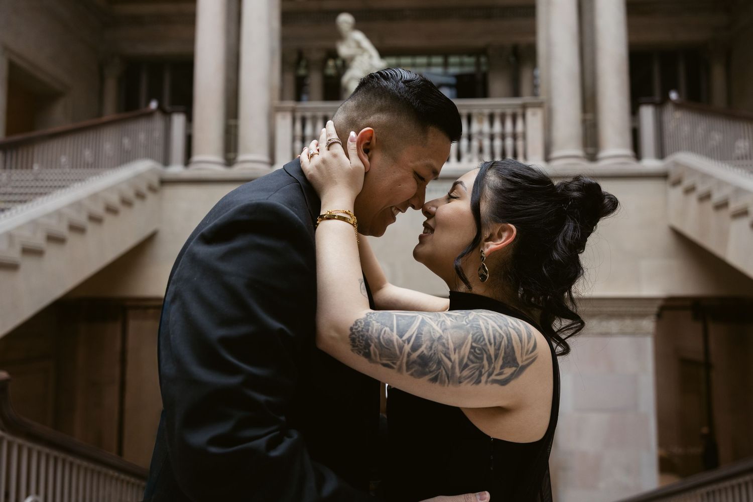 Romantic couple embracing in a museum hallway with elegant columns and classical architecture.