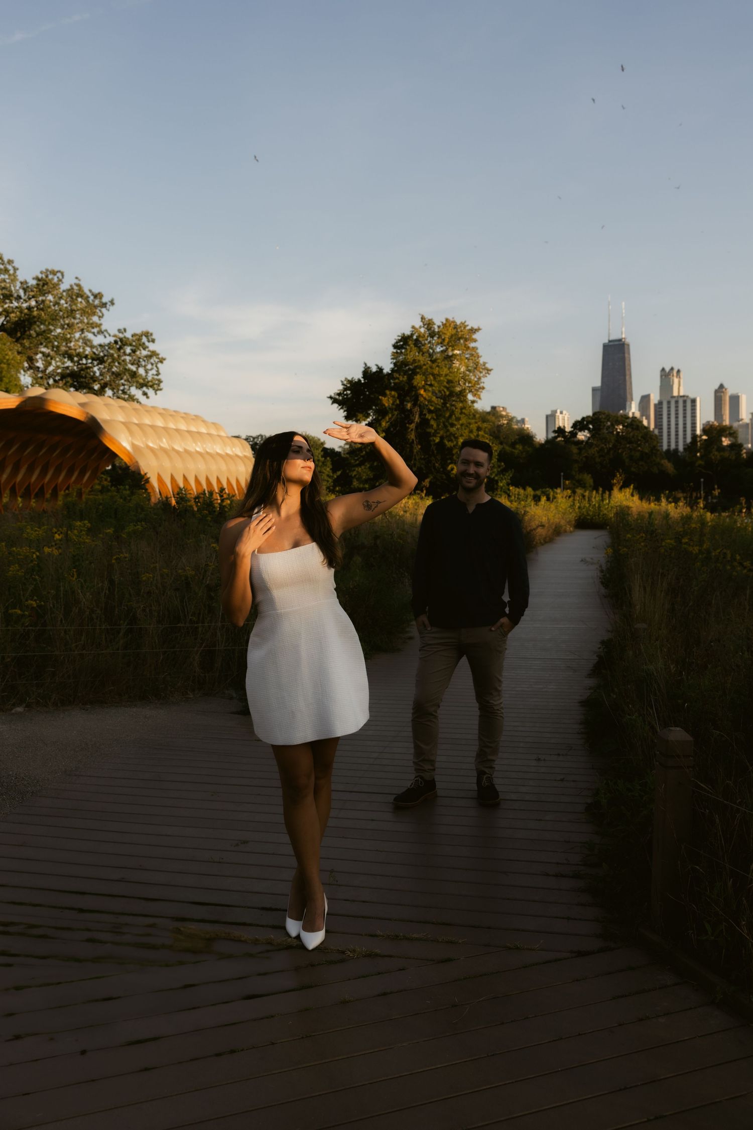 Silhouettes of a couple dancing on a deck at dusk with urban buildings in the background.
