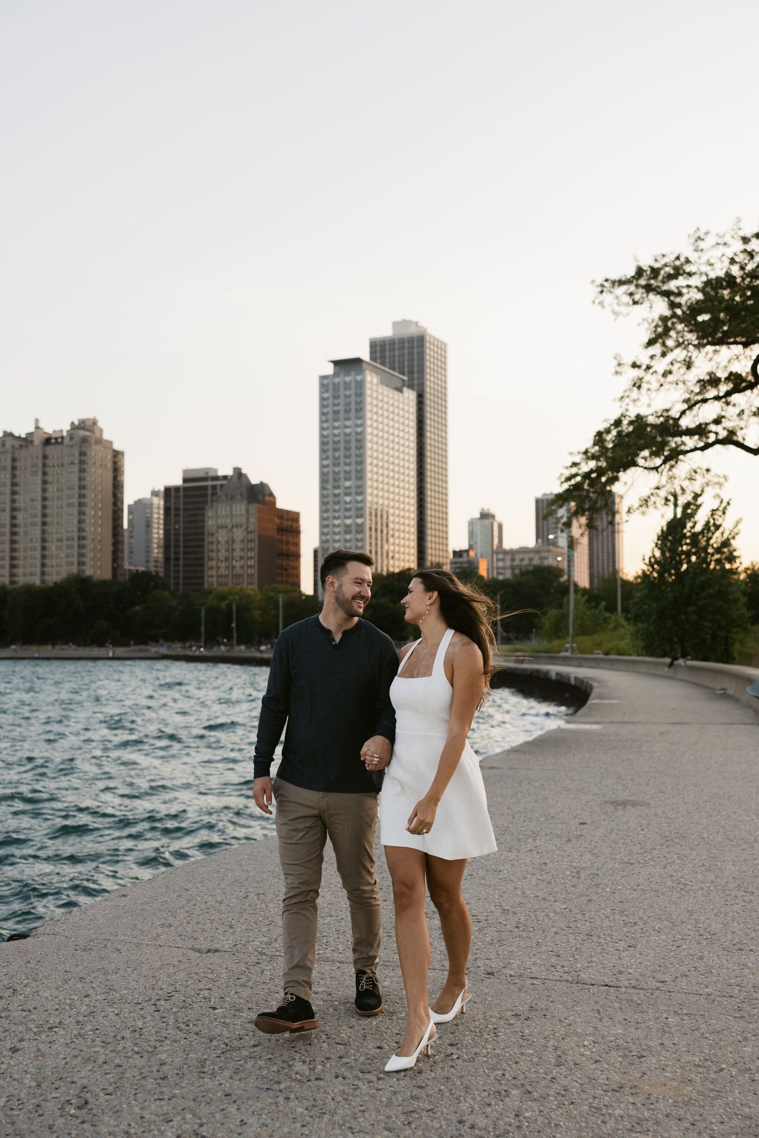 Couple walking along North Avenue Beach with Chicago skyline in background.
