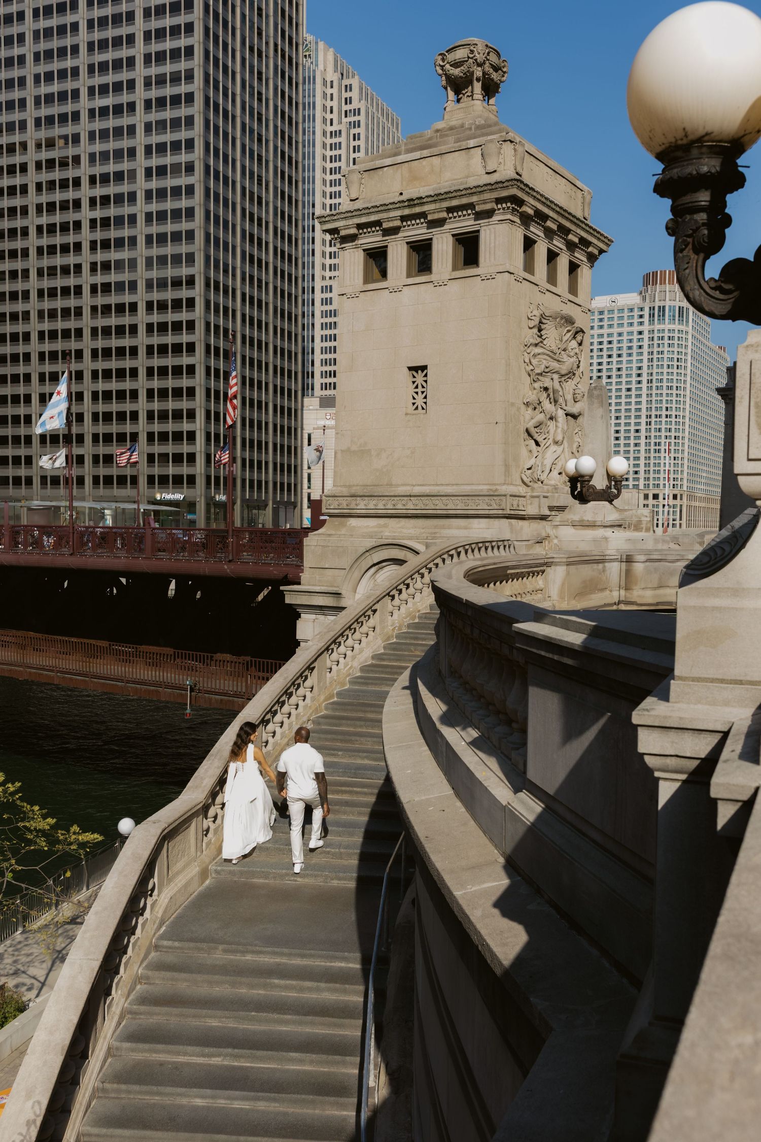 A couple walks up ornate stone steps of a historic building with Chicago skyscrapers in the background.