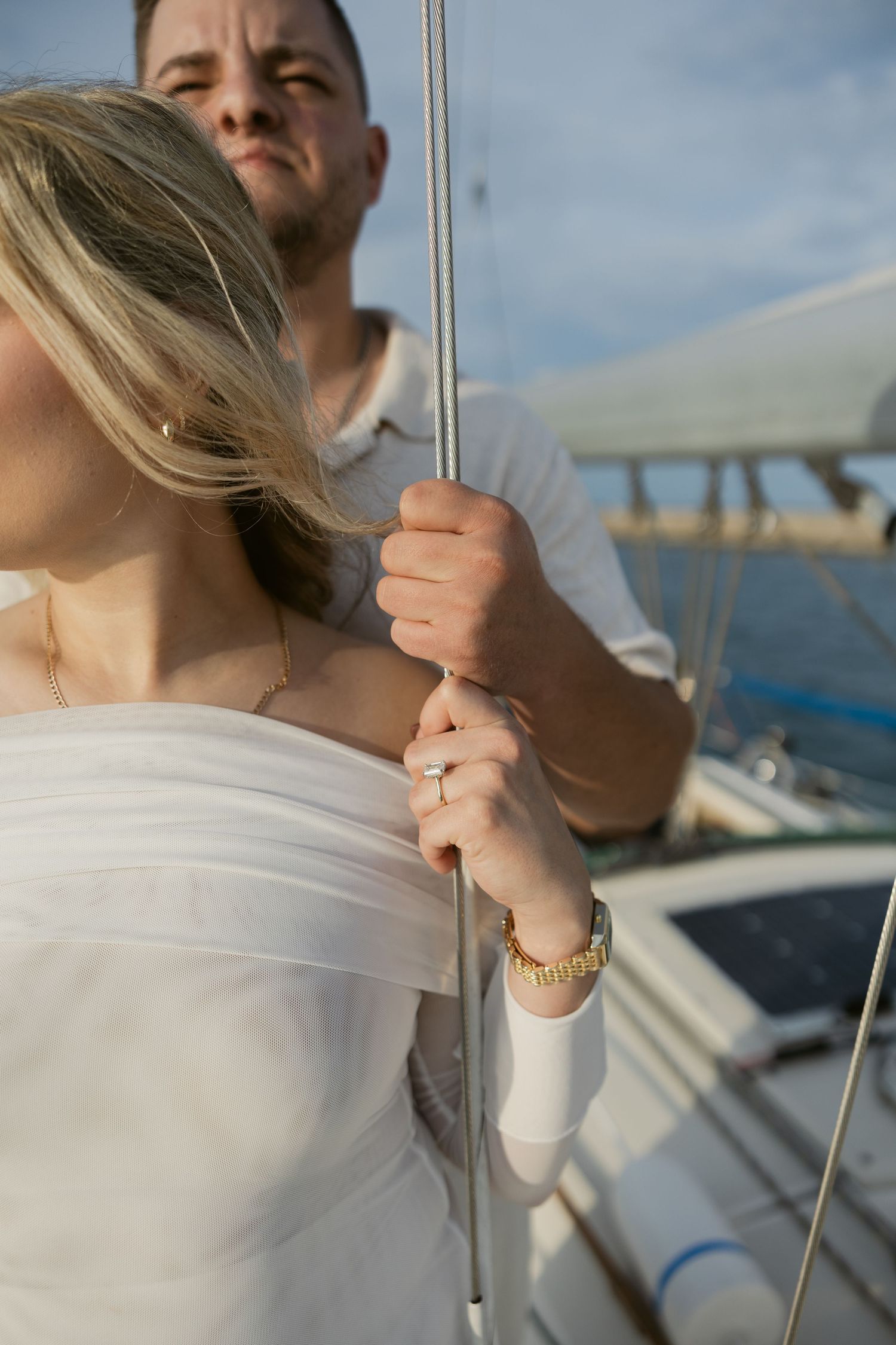 Close-up details of hands holding yacht rigging with jewelry visible.