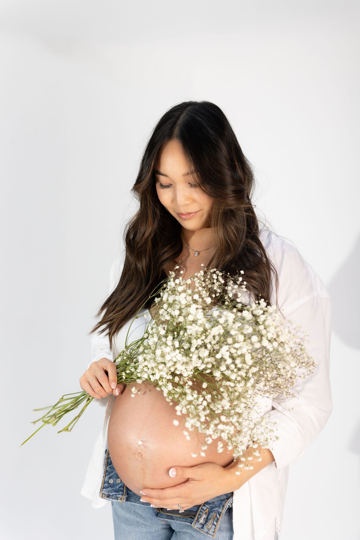 Elegant maternity photos with baby's breath flowers and casual white shirt styling.