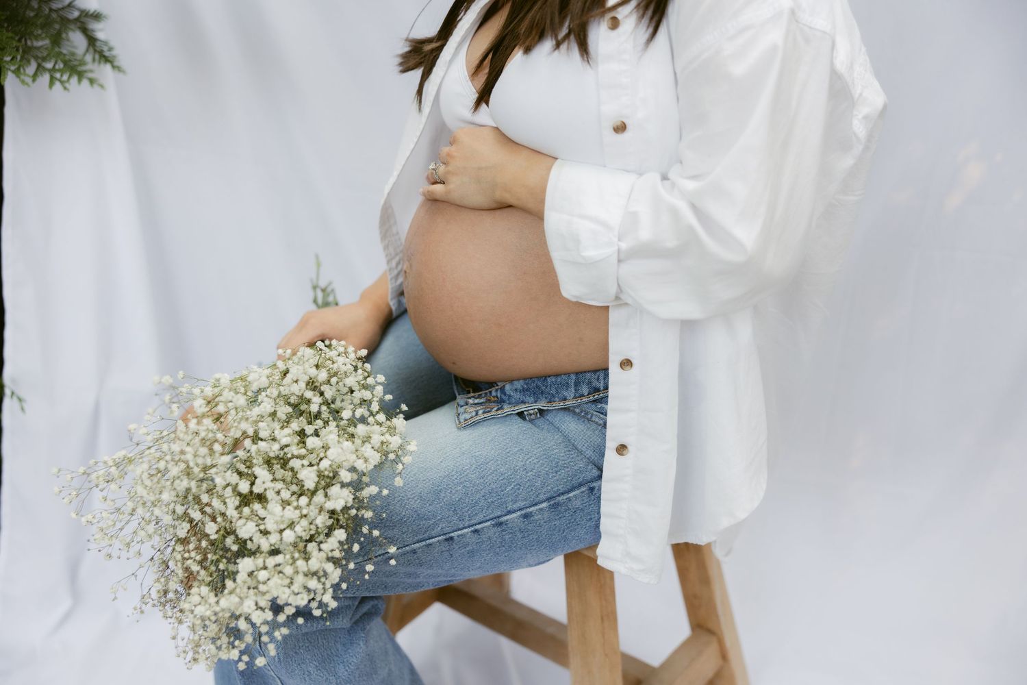 Candid maternity poses against white backdrop with delicate floral accents.