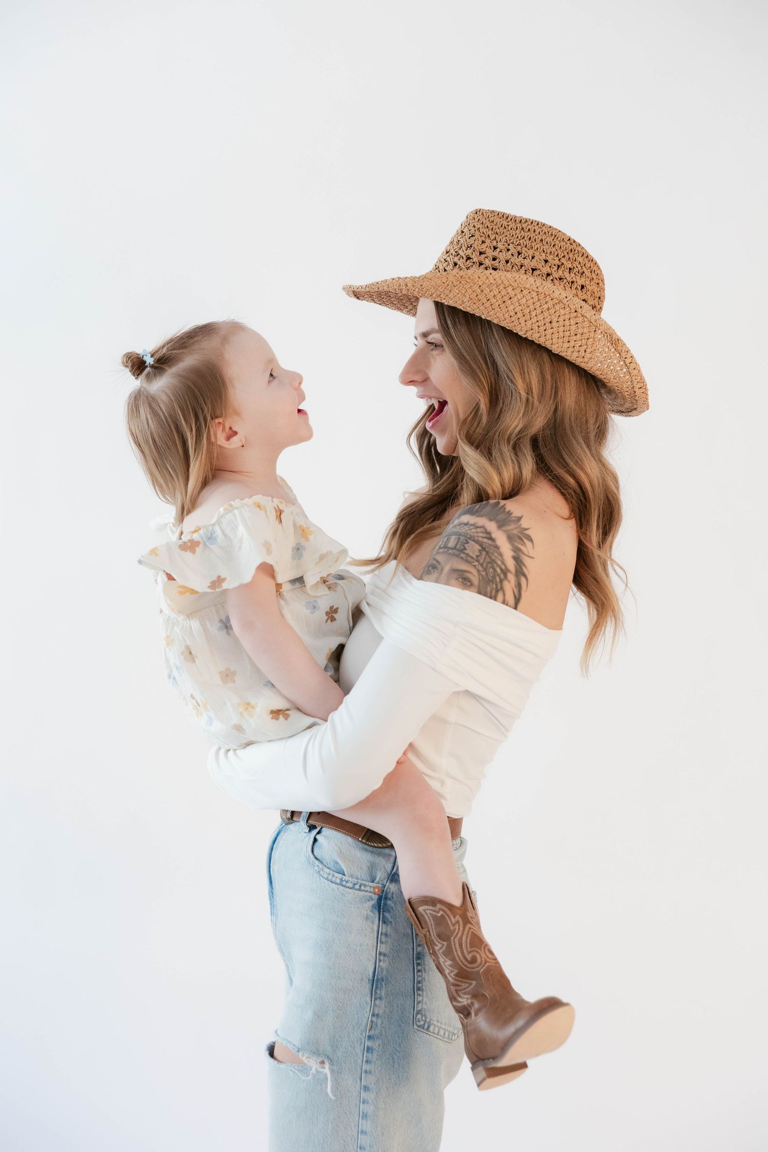 Sweet playful moment captured against white backdrop shows parent lifting child in joyful embrace.