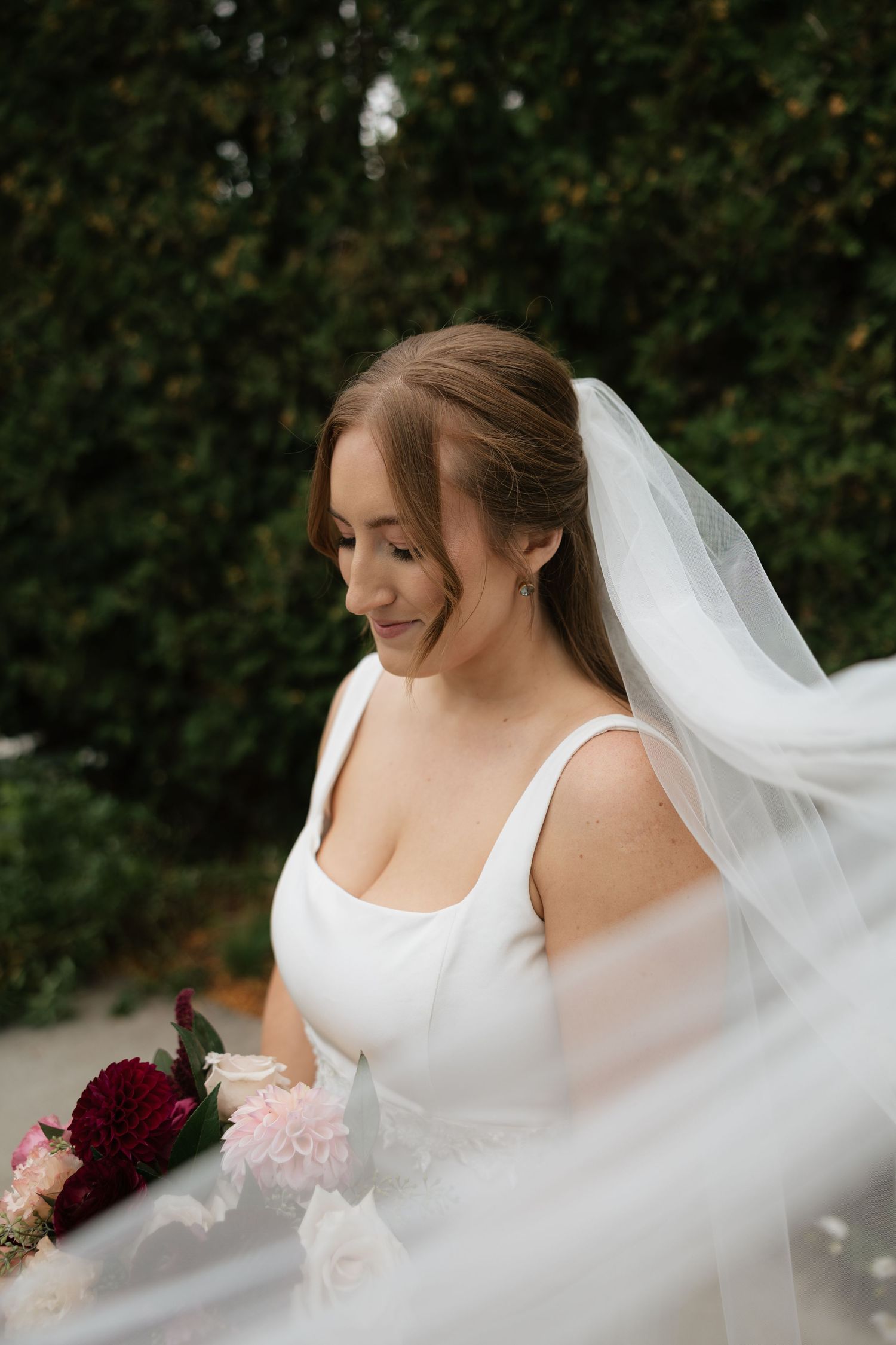 A flowing white wedding veil catches the breeze as it billows gracefully around the bride in an outdoor setting.