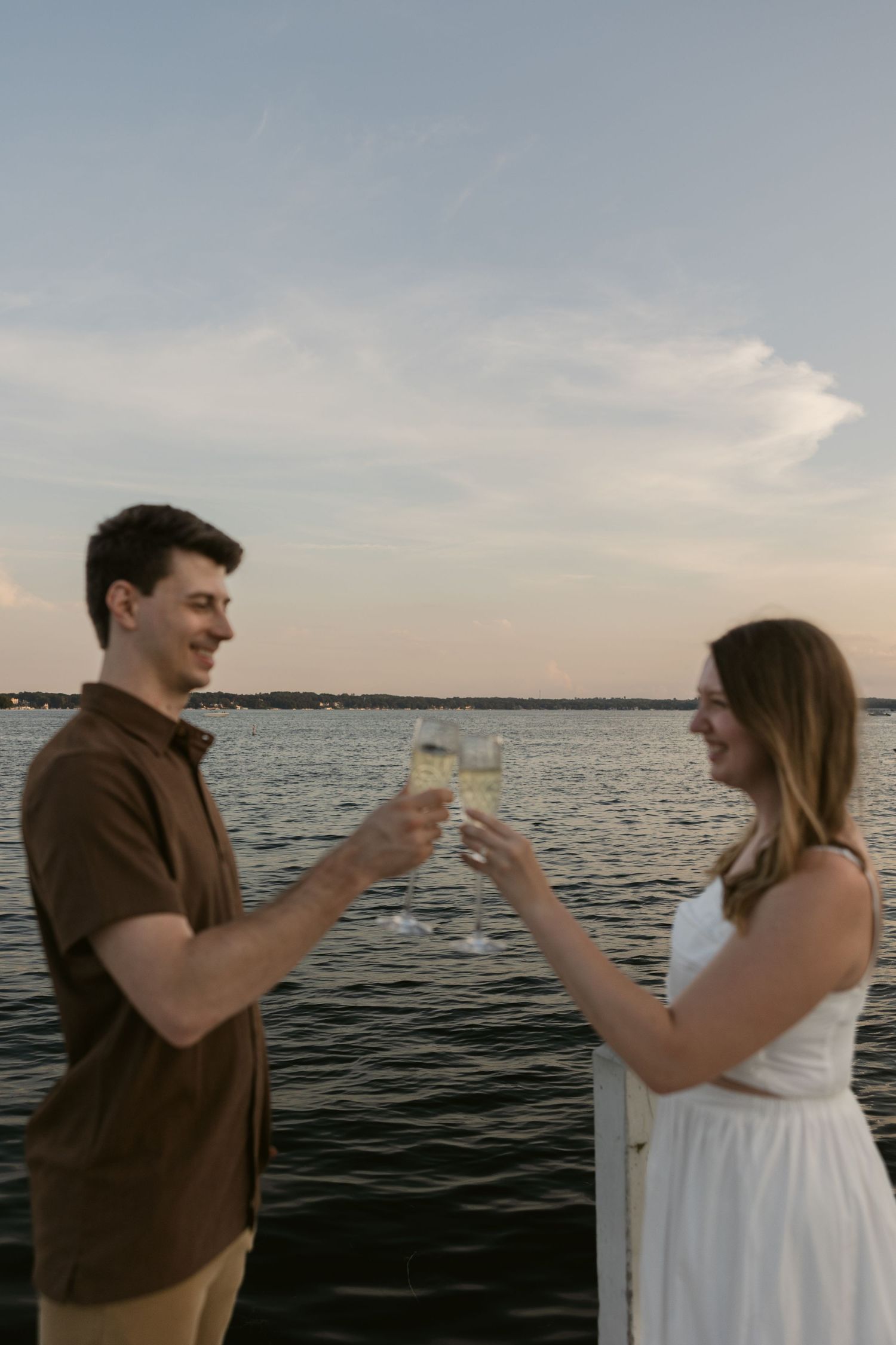 A couple toasts with wine glasses while enjoying a waterfront sunset on a pier.