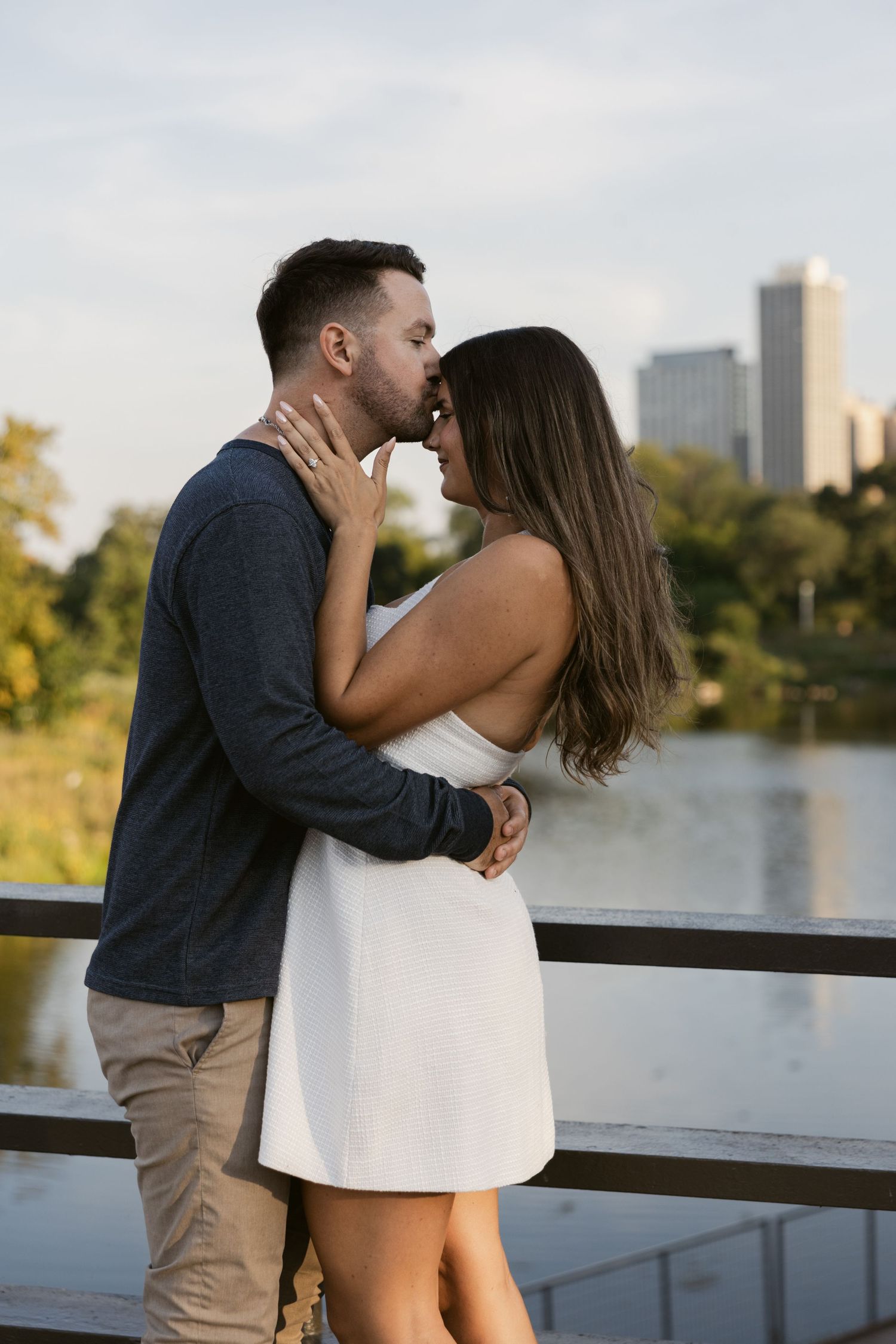 A tender moment shared between a couple on a deck overlooking a city skyline at dusk.