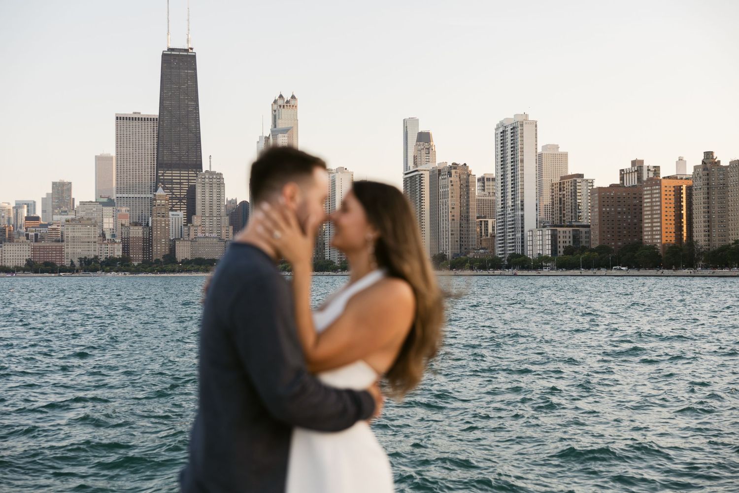 A couple shares an intimate moment at North Avenue Beach with Chicago's iconic skyline in the background.