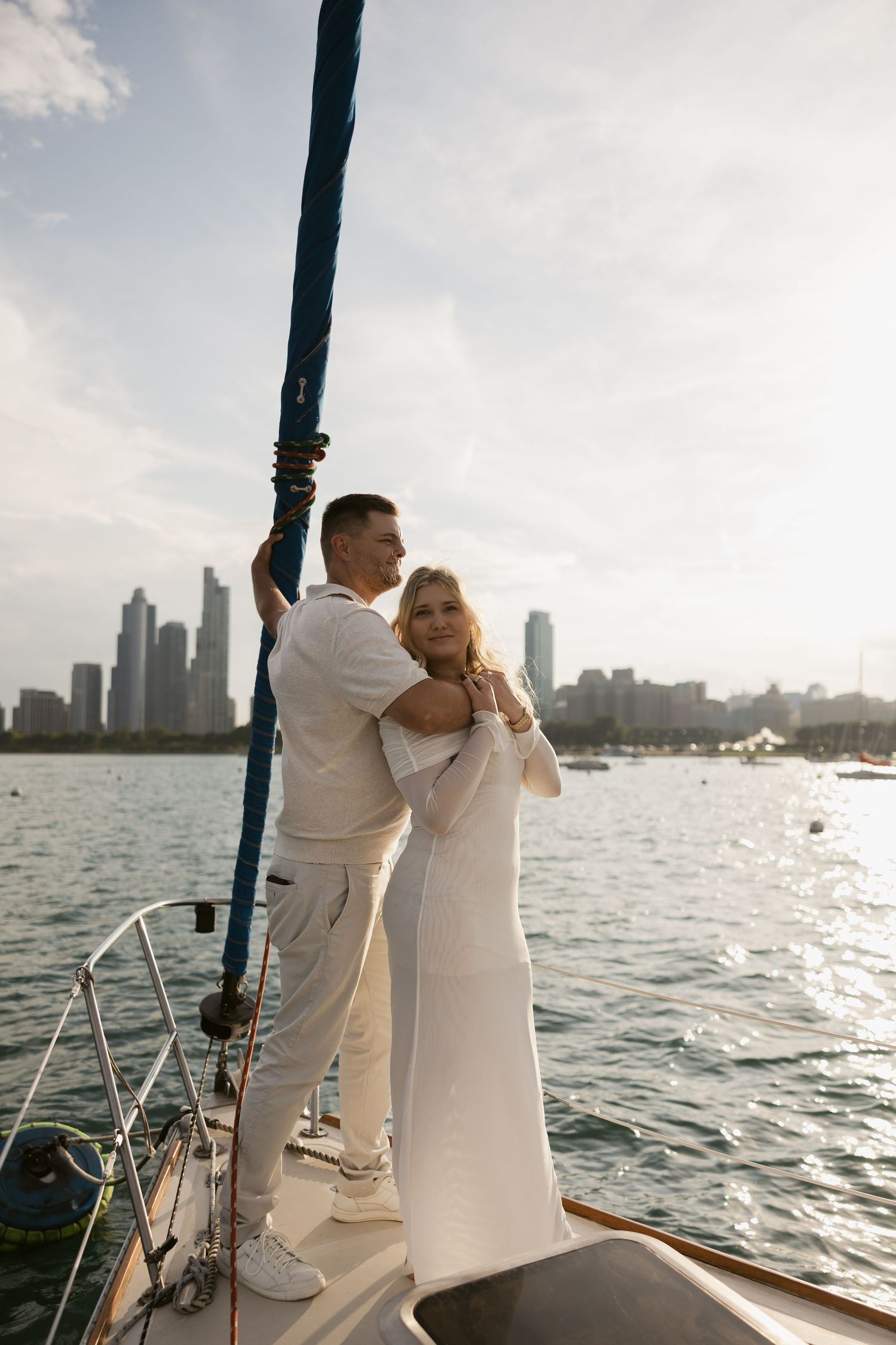 A couple in all white outfits sharing a romantic moment on a sailboat with Chicago skyline in the background at sunset.