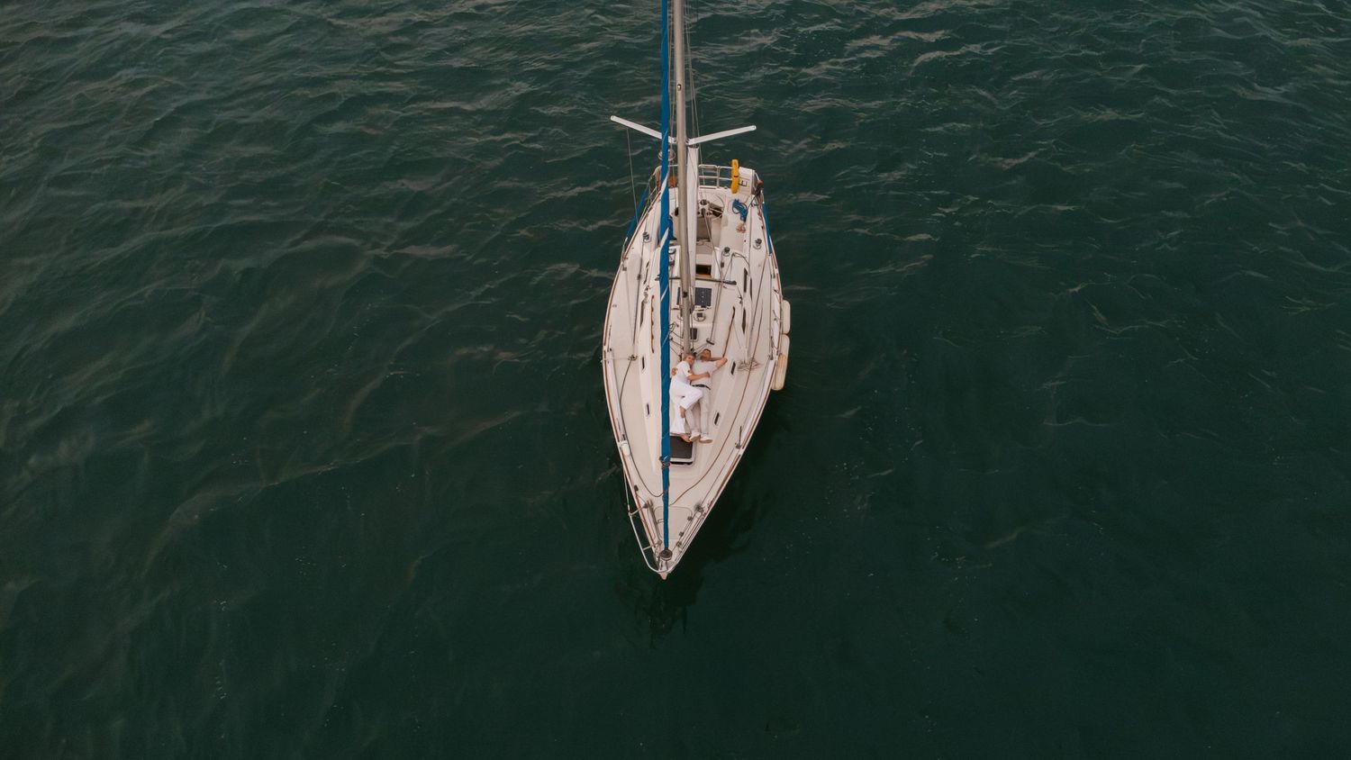 Aerial view of sailboats on dark water creating parallel lines against the surface.