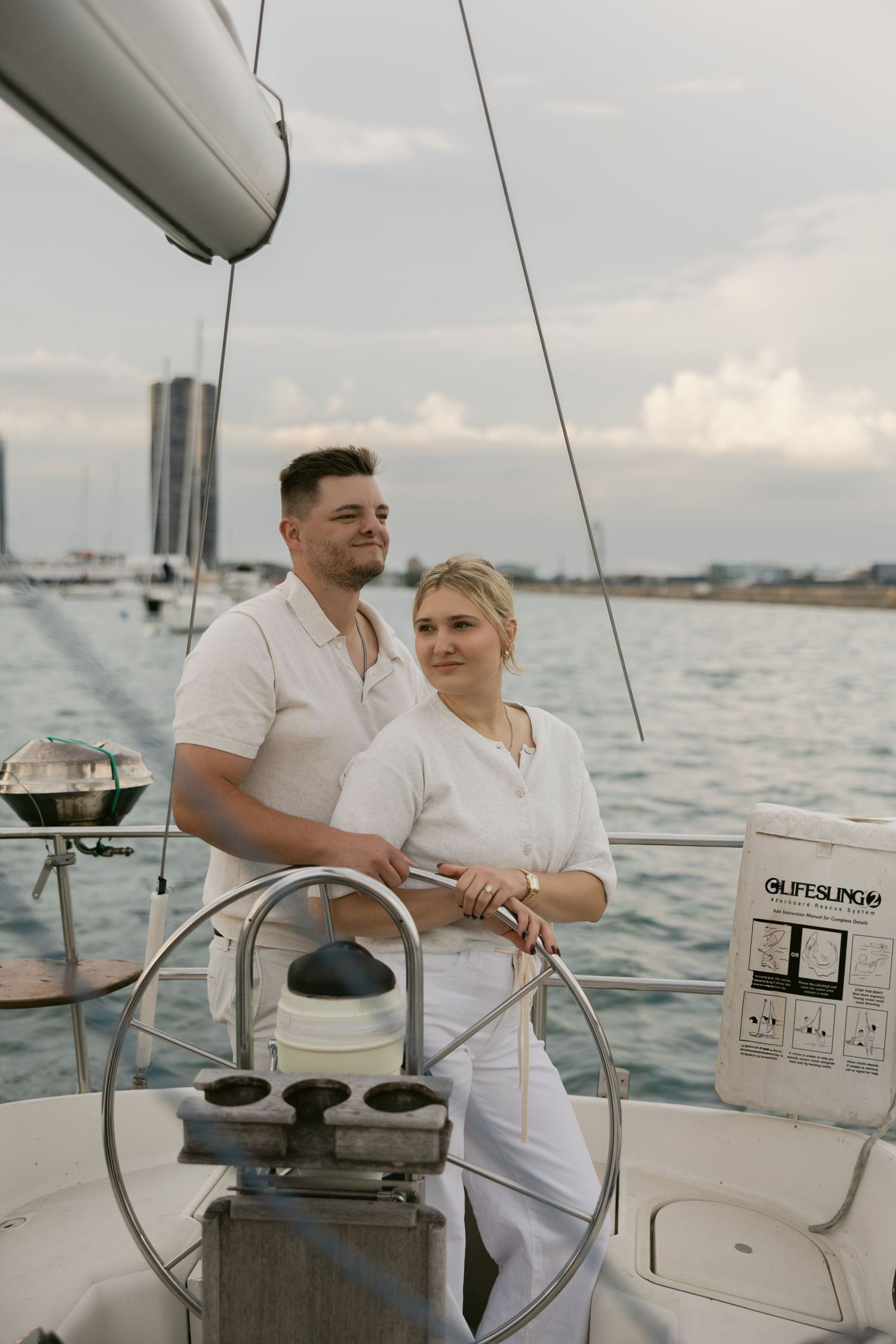 Nautical-themed couple's photoshoot on a sailboat with urban waterfront views.