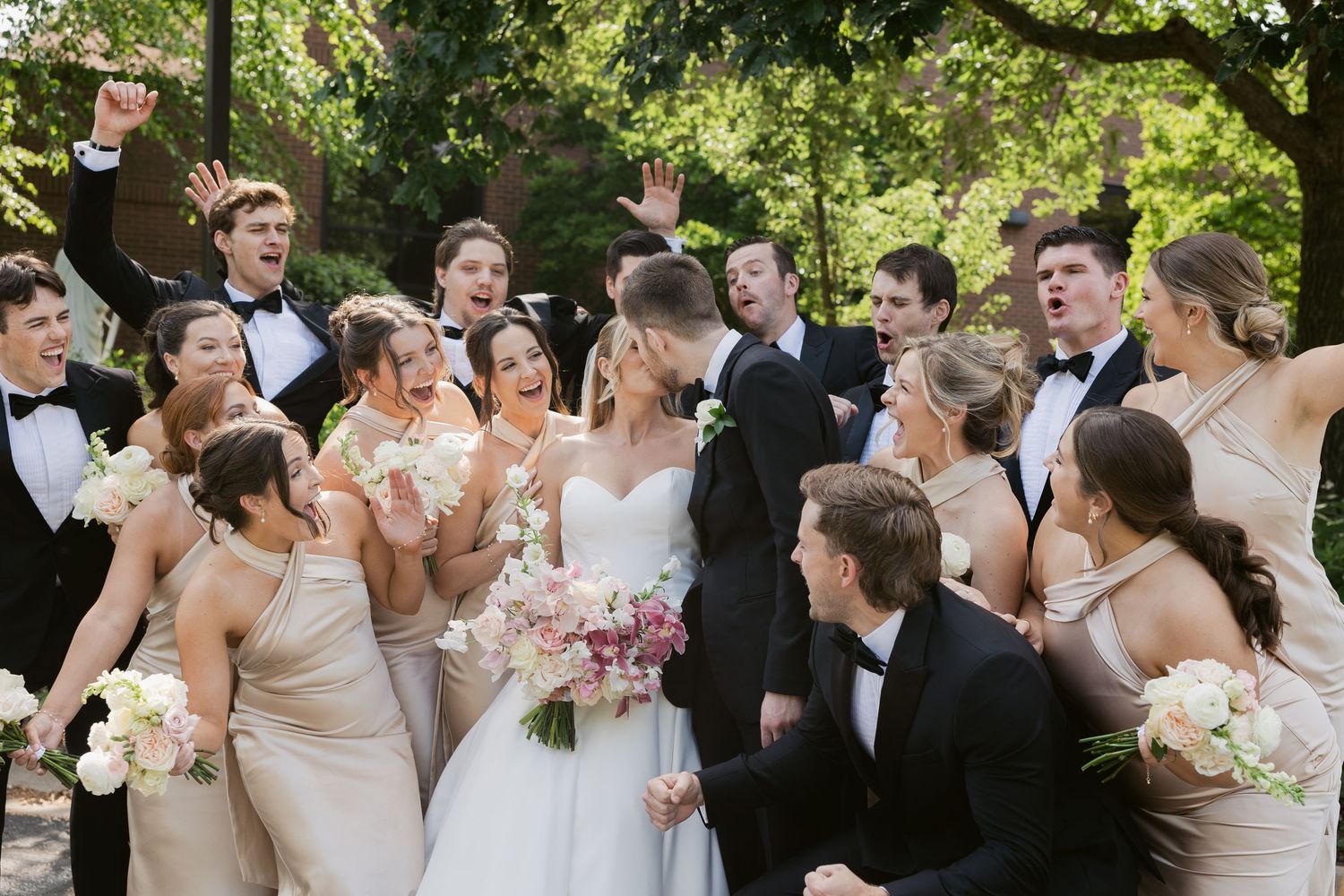 Wedding party celebrates joyfully together in an outdoor garden setting.