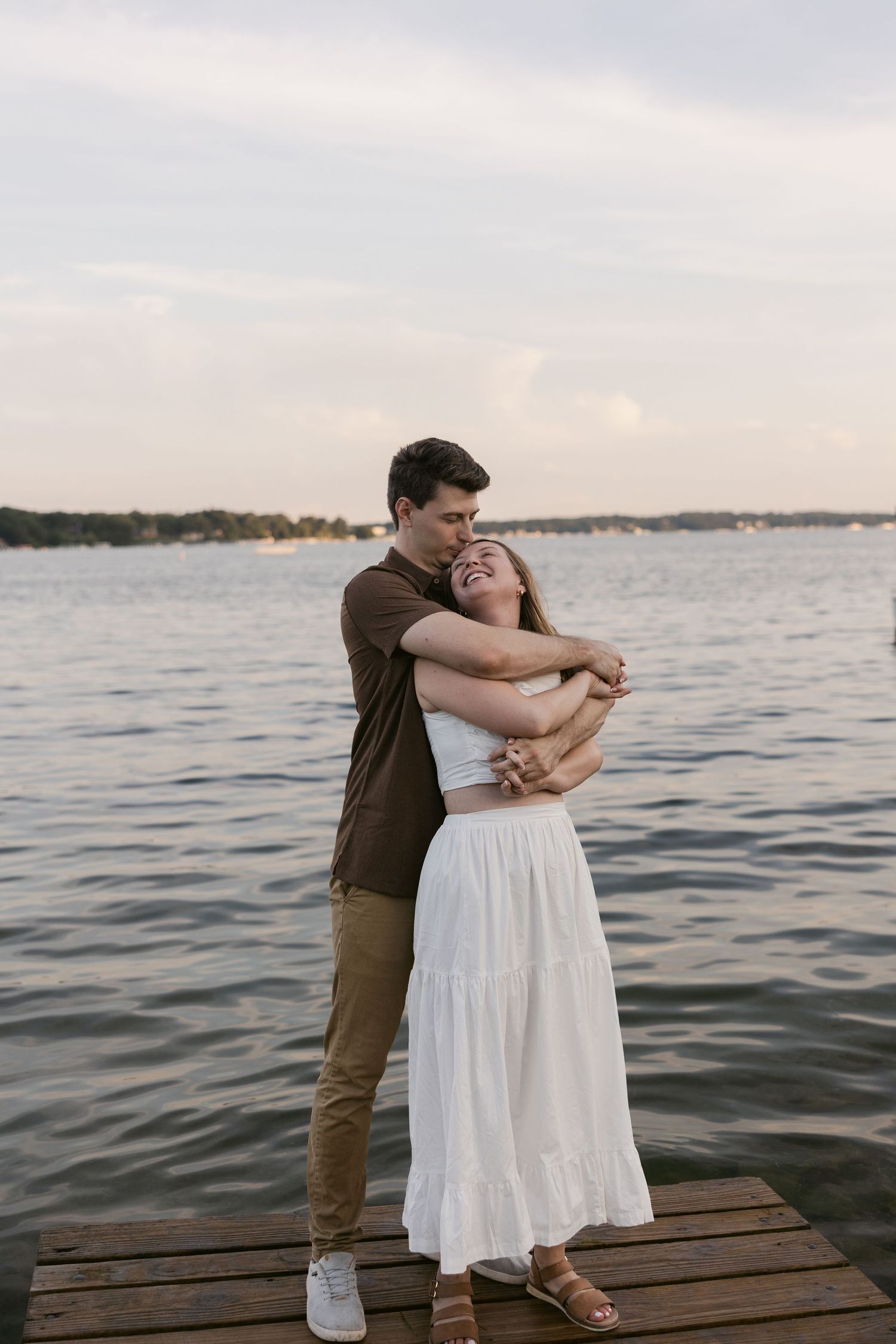 A couple embraces on a wooden dock by the water during sunset.