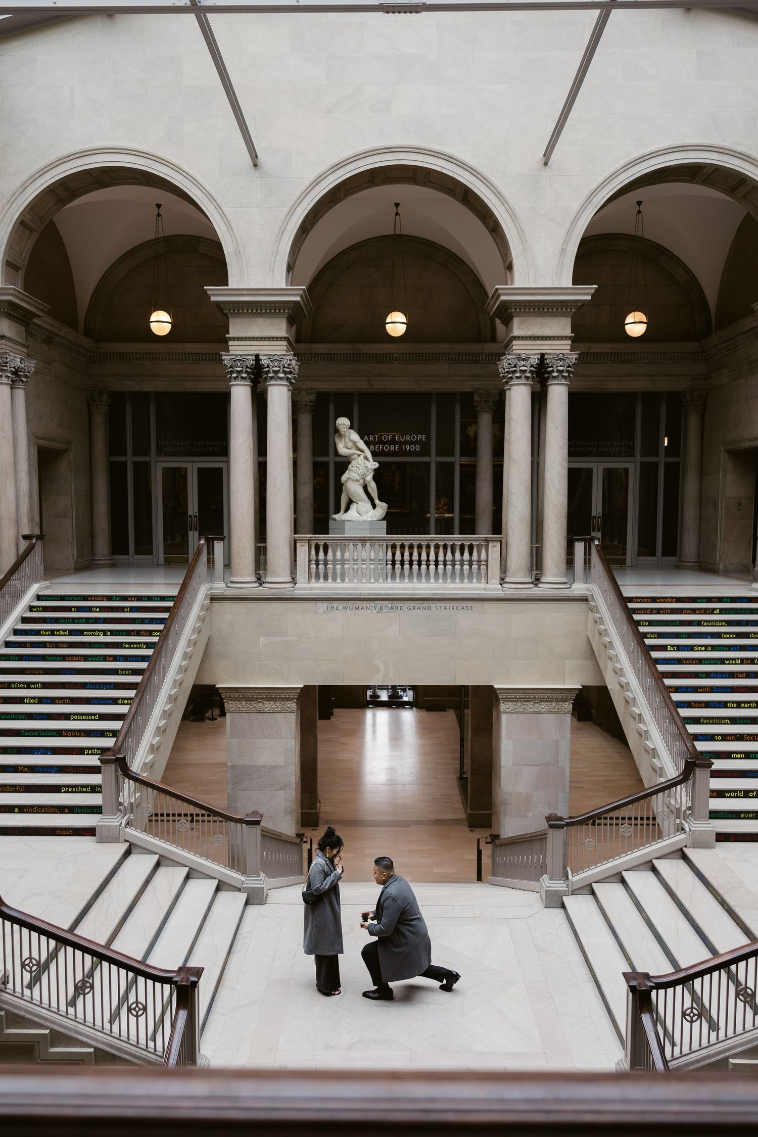 A proposal scene on a grand marble staircase with classical architecture and statue.