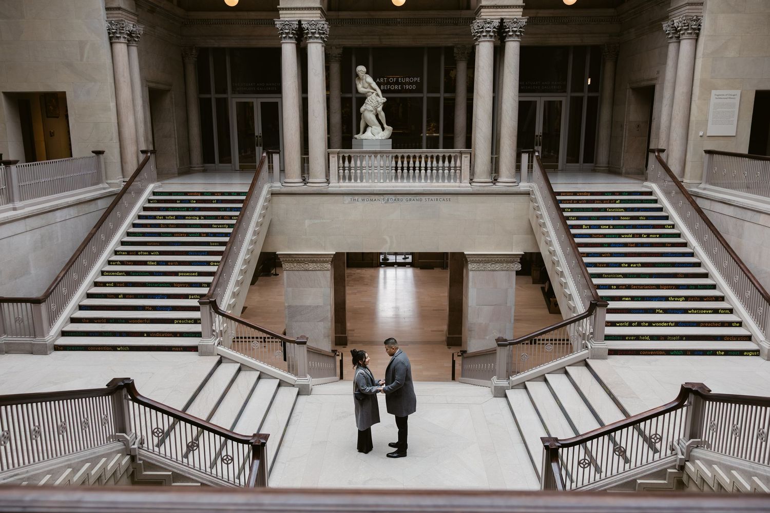 An elegant museum interior featuring symmetrical staircases and classical architecture with marble columns.