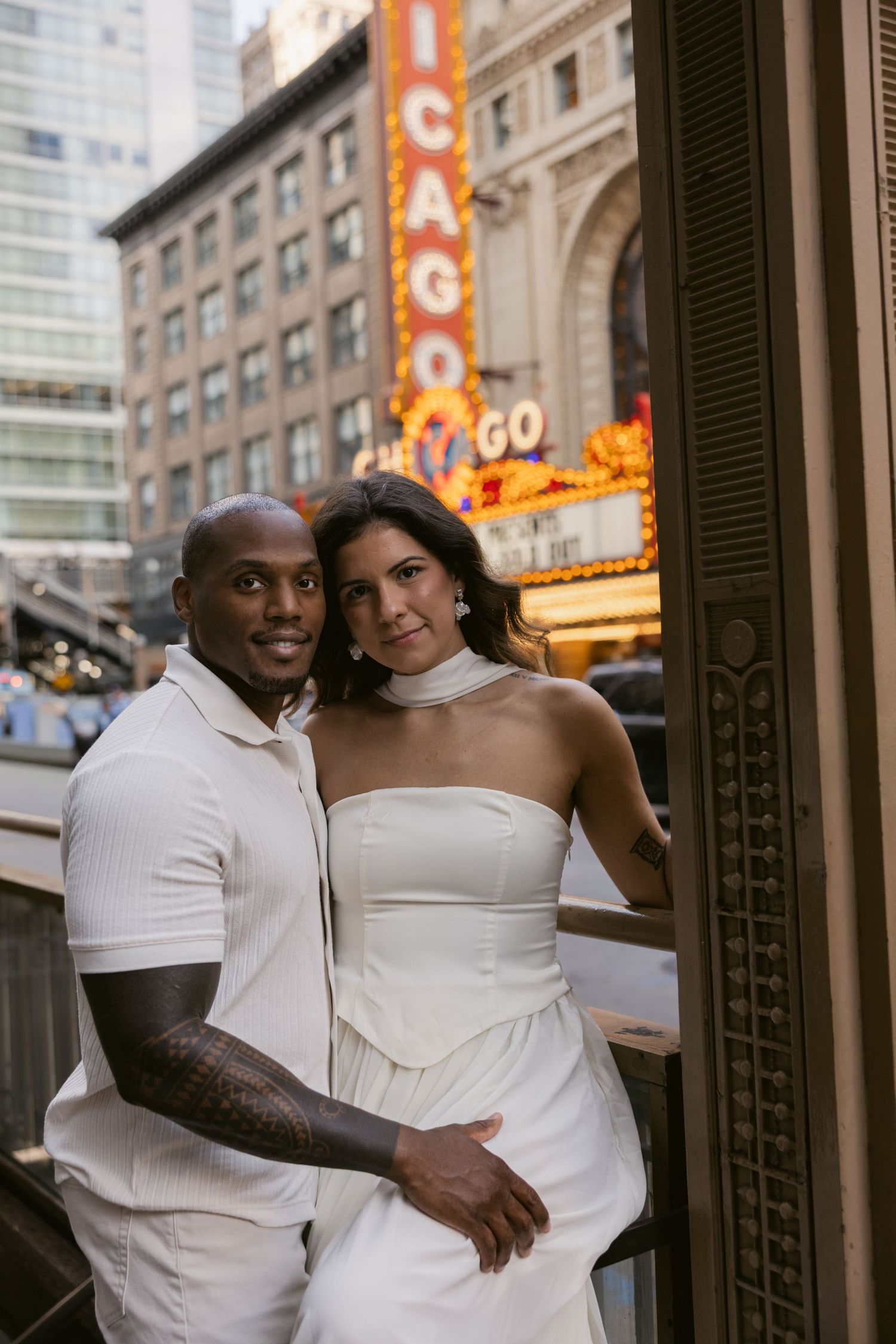 A couple in matching white outfits sharing romantic moments against an urban backdrop.