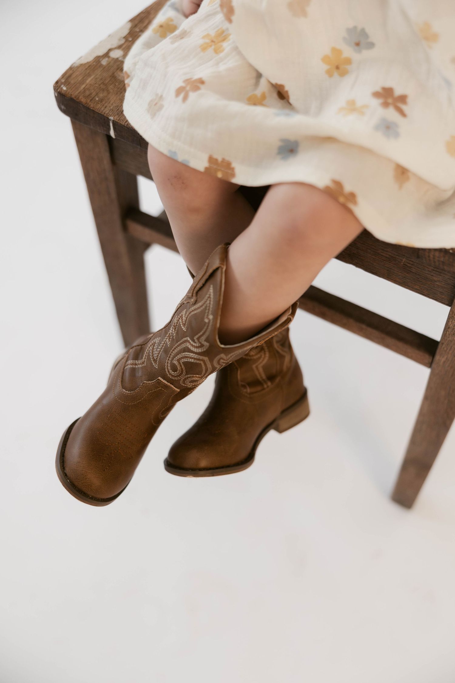 Close-up of brown leather cowboy boots on child sitting in wooden chair.