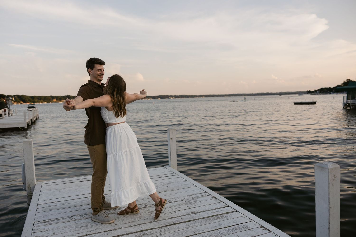 A couple dances together on a wooden dock by the ocean at sunset.