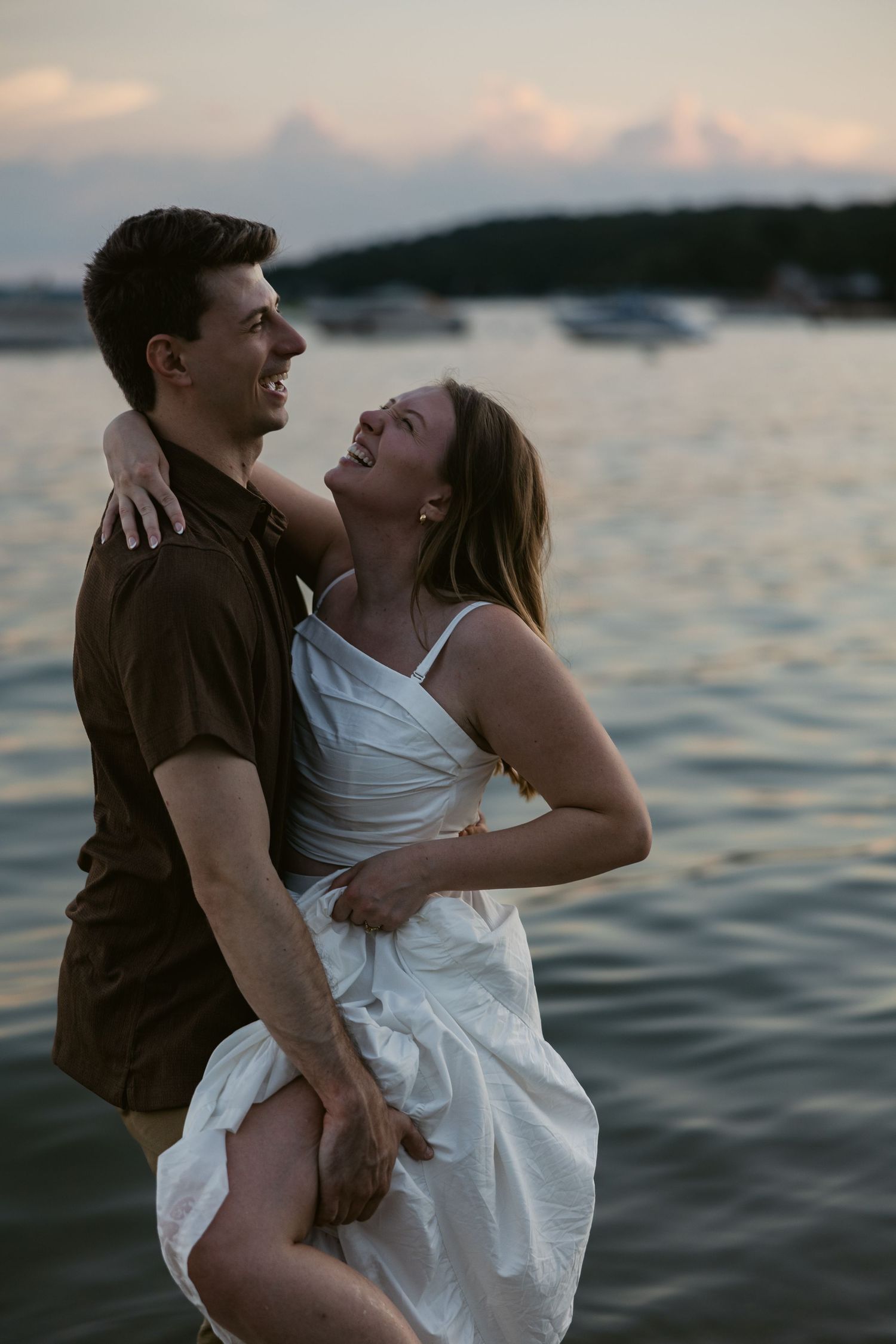 A couple embraces playfully in the ocean water during golden hour.
