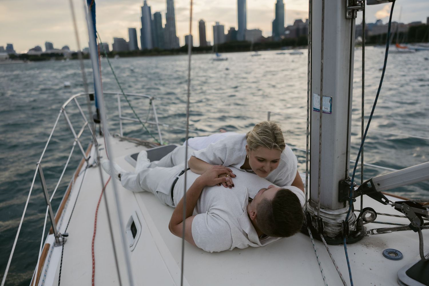 Romantic nautical photoshoot on sailboat with city skyline visible in distance.